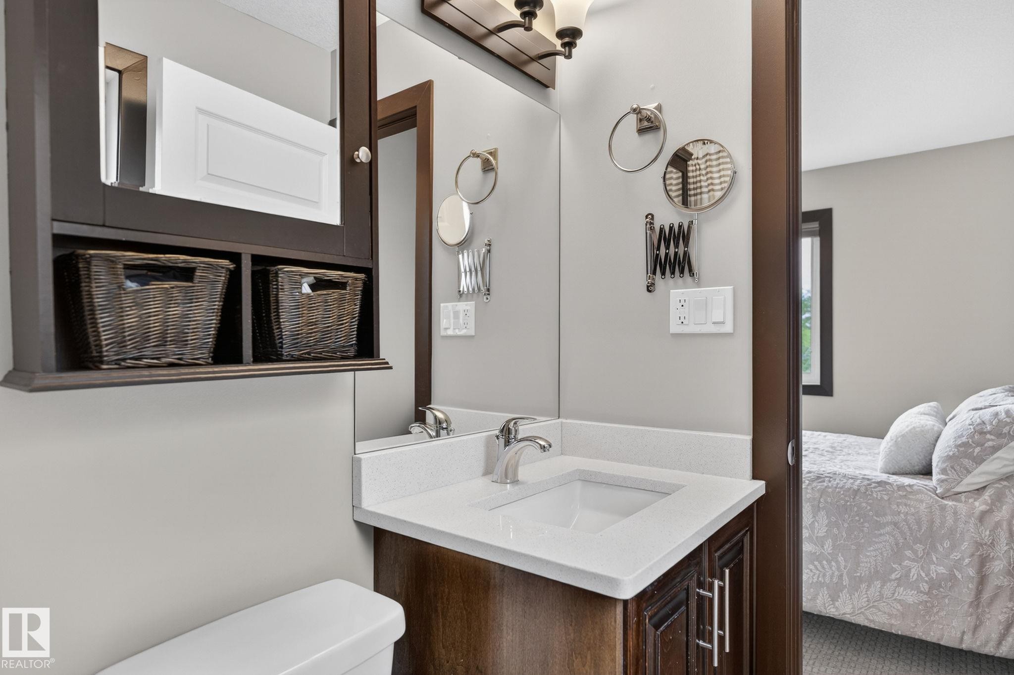 Vanity with a white countertop and integrated sink, complemented by a dark wood-finish cabinet and medicine cabinet with open shelving - 8506 80 Avenue, Edmonton, AB