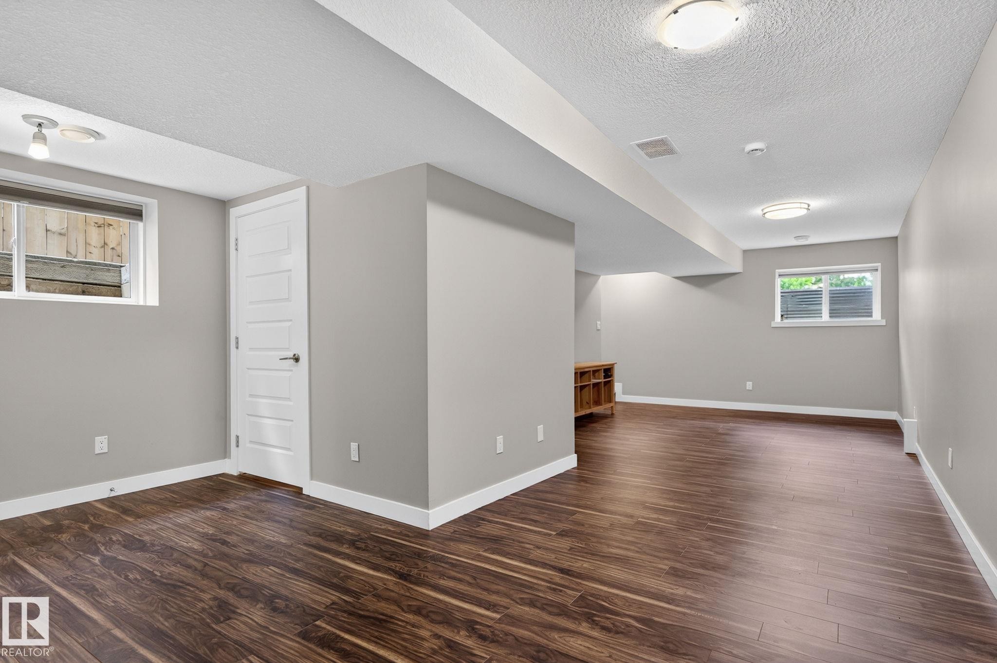 Finished lower level featuring wood-finish flooring, neutral paint, white trim, and multiple windows - 8506 80 Avenue, Edmonton, AB