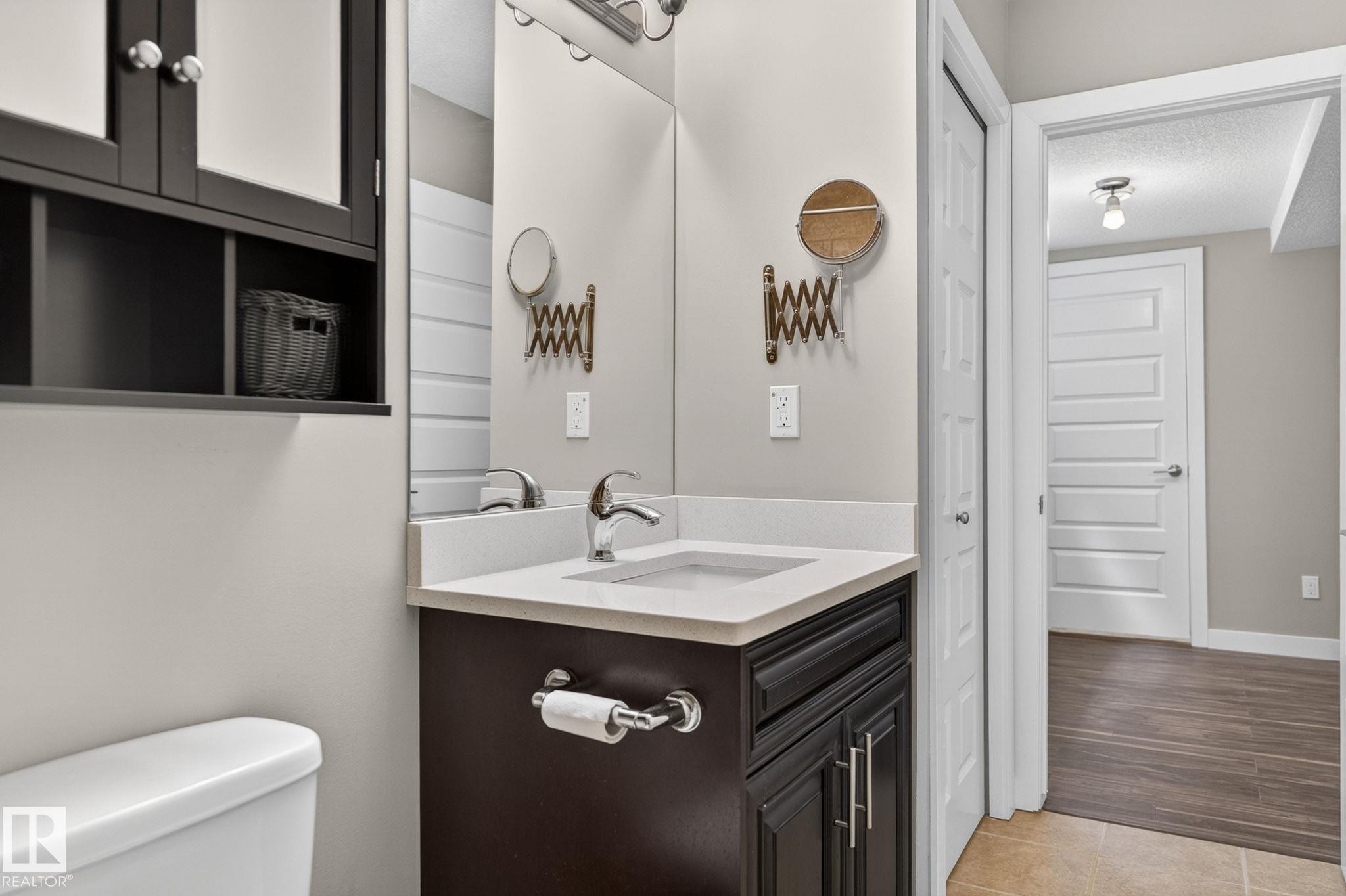 Bathroom vanity featuring a dark wood-finish cabinet with silver-tone hardware, a white undermount sink, and a light-toned countertop - 8506 80 Avenue, Edmonton, AB