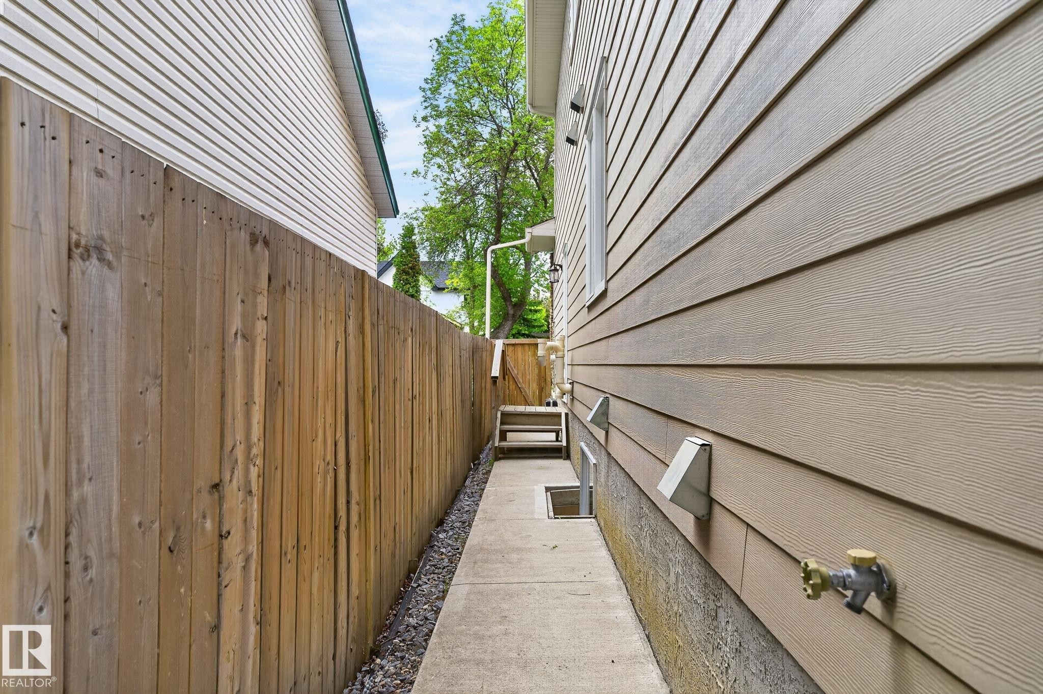 Side yard featuring concrete pathway, wood fence, and light-toned horizontal siding - 8506 80 Avenue, Edmonton, AB