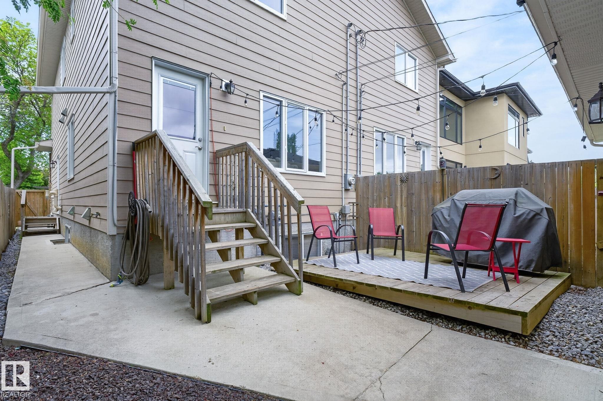 Rear exterior featuring a wood deck, concrete patio, wood fence, and string lighting - 8506 80 Avenue, Edmonton, AB