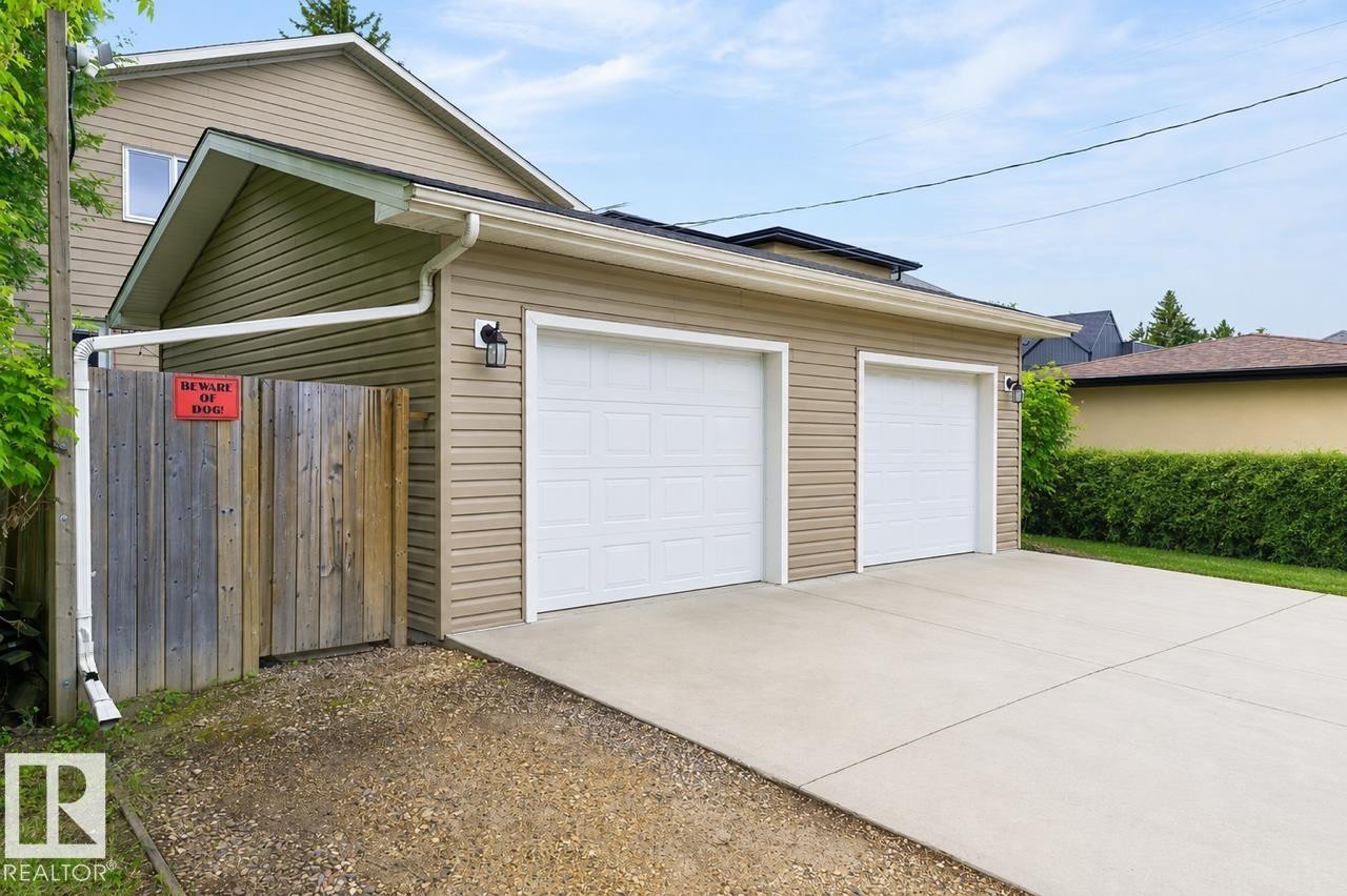 Attached two-car garage with white paneled garage doors, tan horizontal siding, exterior lighting fixture, and concrete driveway - 8506 80 Avenue, Edmonton, AB
