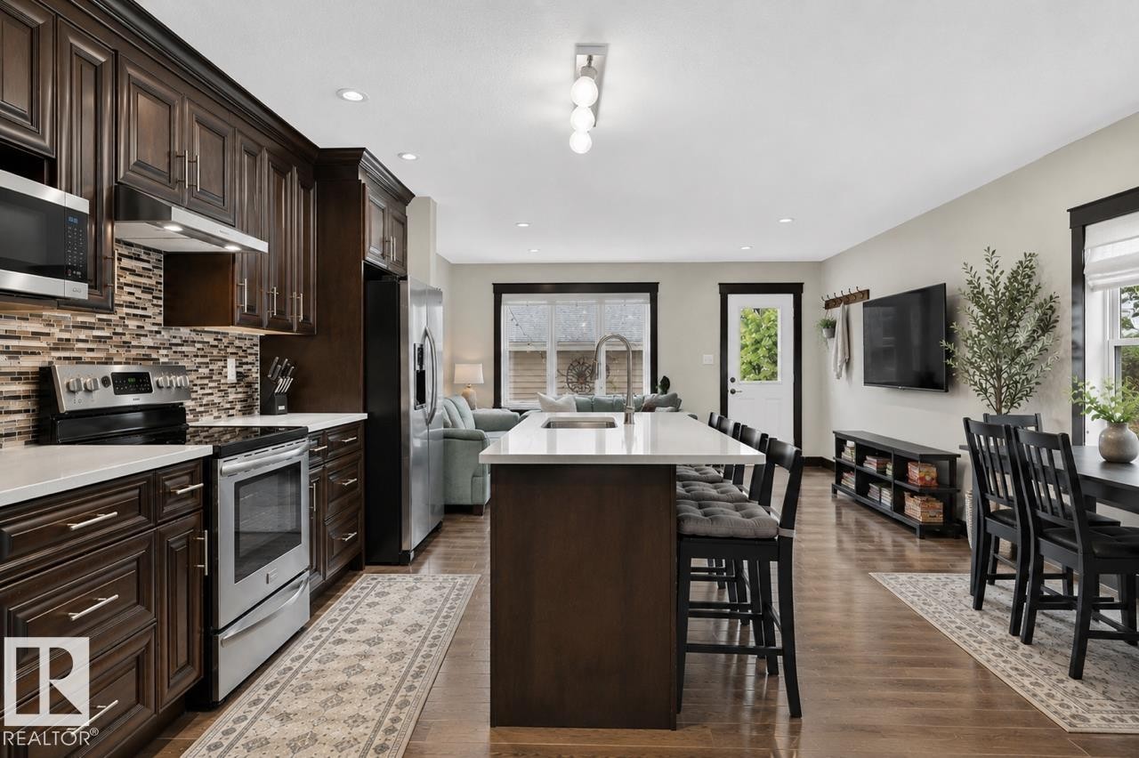 Spacious kitchen featuring dark wood cabinetry, stainless steel appliances, a tile backsplash, and a large island with seating - 8506 80 Avenue, Edmonton, AB