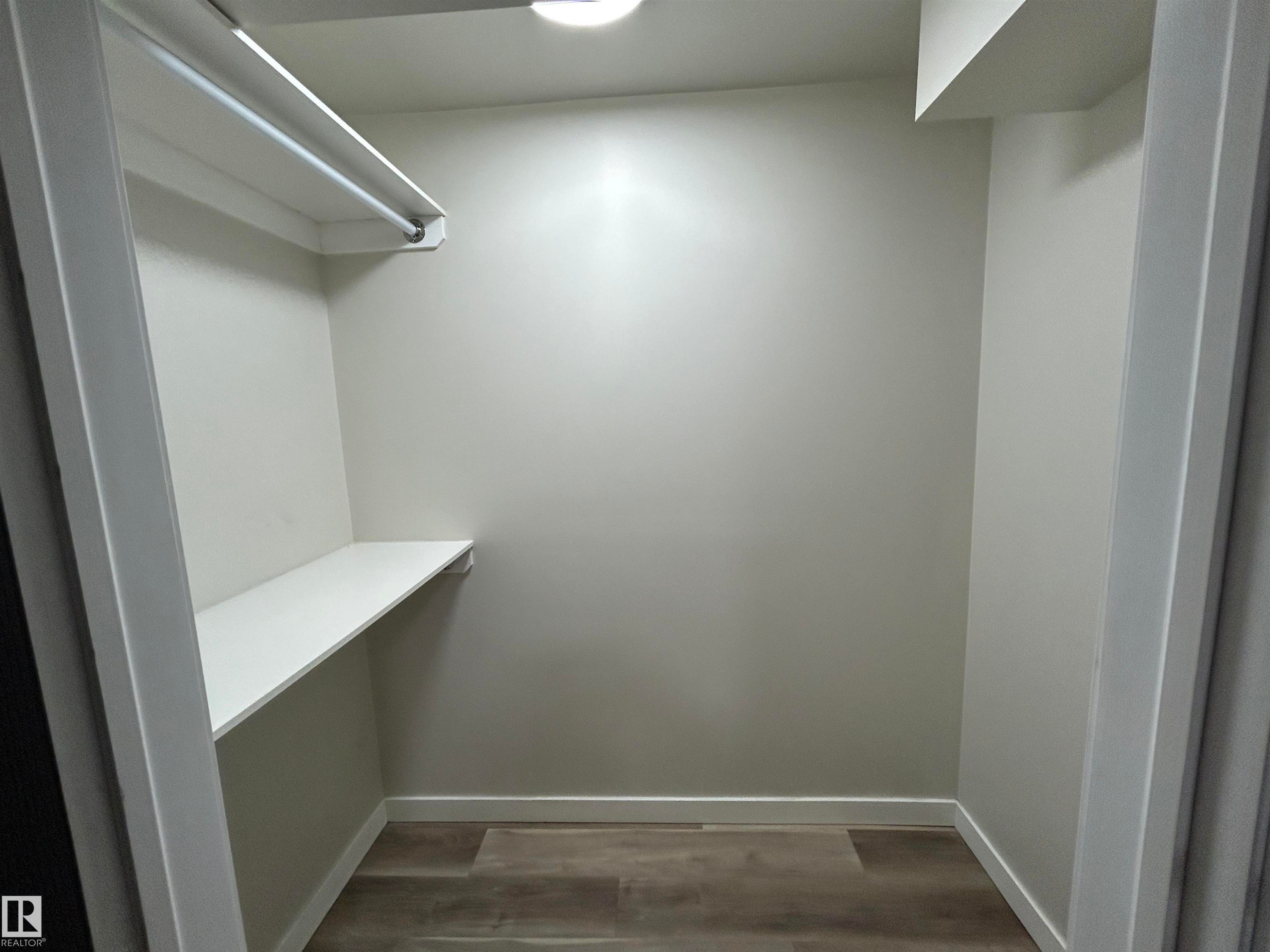 Spacious walk-in closet featuring light grey walls, wood-finish flooring, a white clothes rod, and a white storage shelf - 10924 30 Street, Edmonton, AB