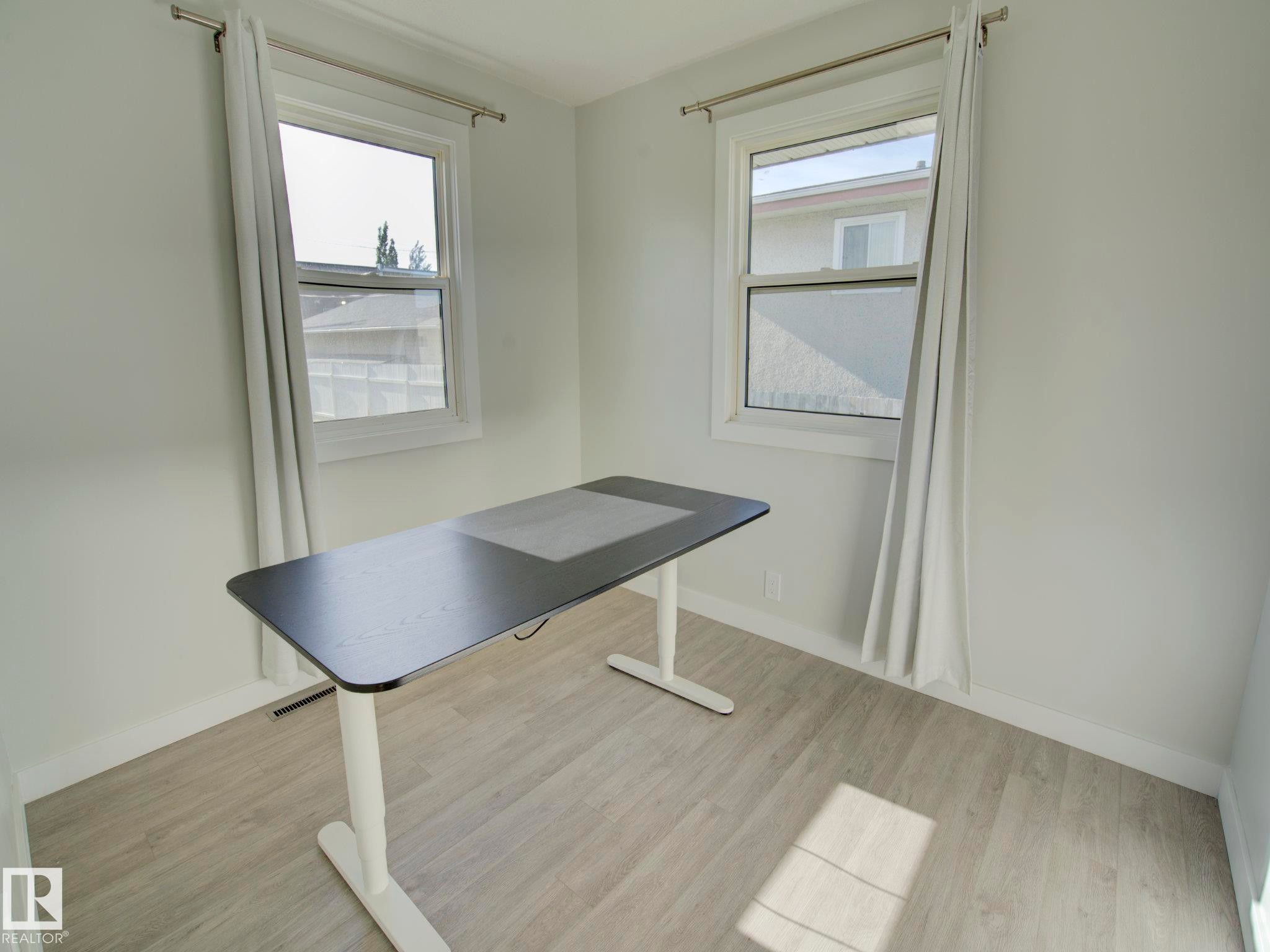 Room featuring light wood-finish flooring, white baseboards, and two windows with white trim - 9909 157 Street, Edmonton, AB