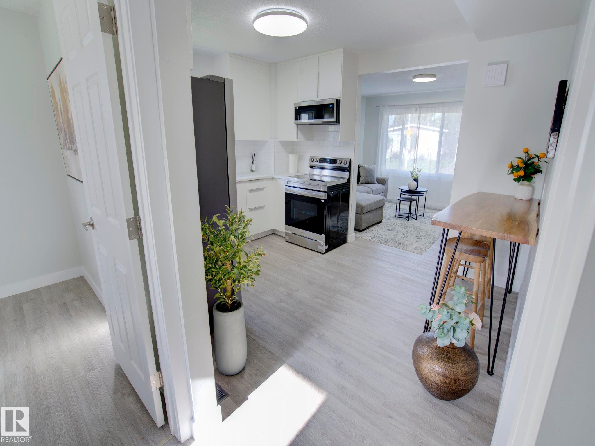 Open-concept kitchen featuring white cabinetry, stainless steel appliances, and light wood-finish flooring - 9909 157 Street, Edmonton, AB