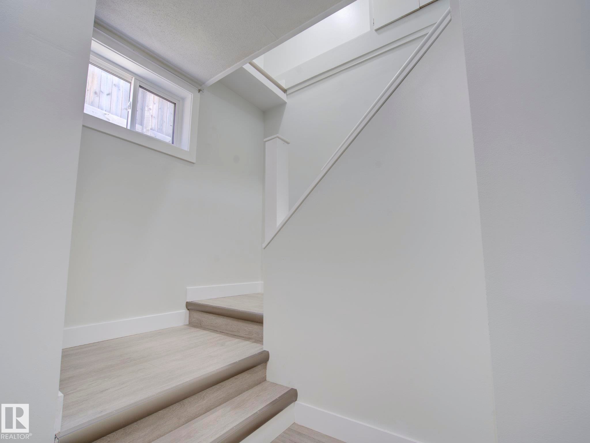 Stairwell featuring light-toned wood-finish flooring, white painted walls, white baseboards, and a contemporary window with natural light - 9909 157 Street, Edmonton, AB