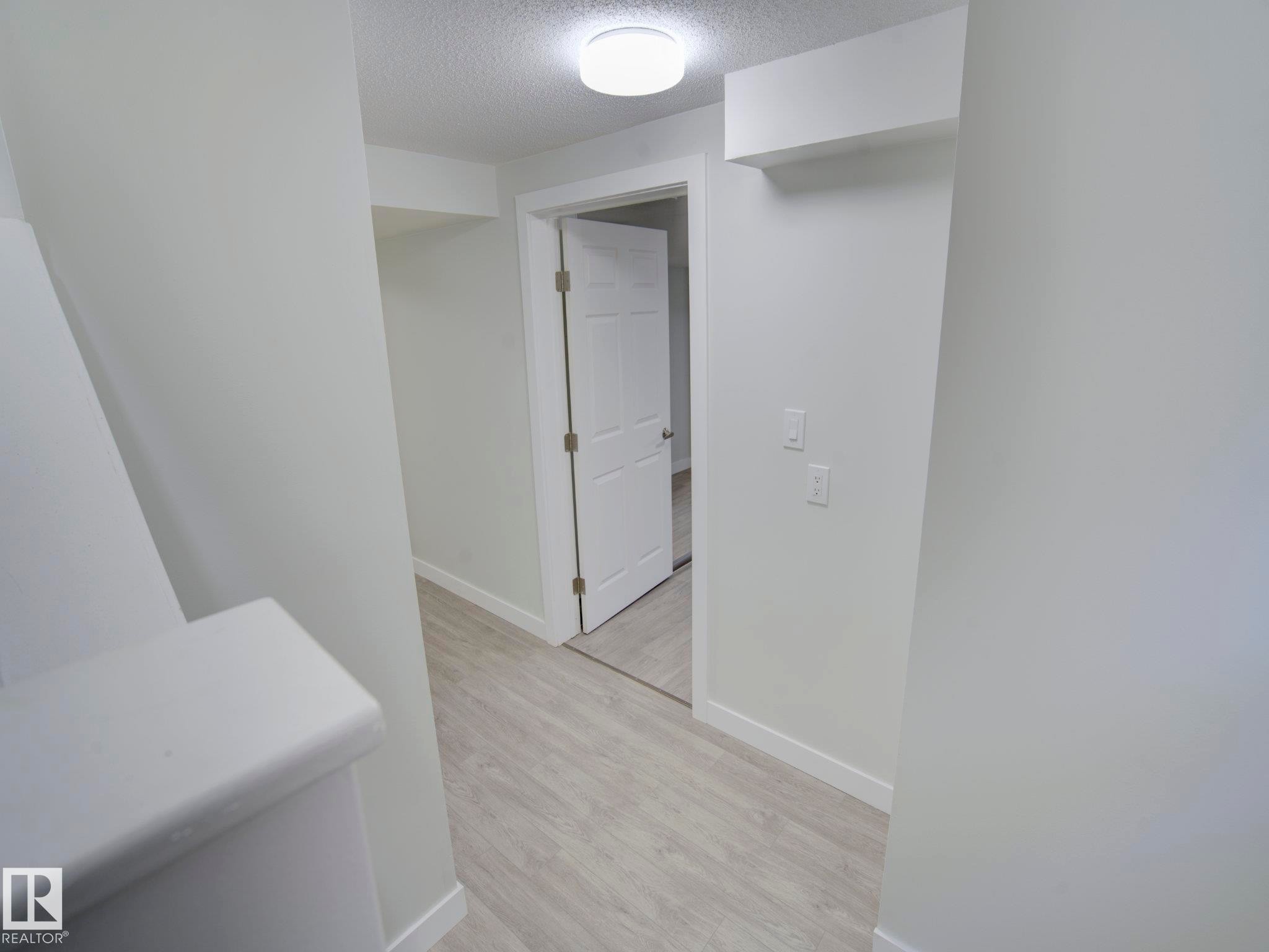 Hallway featuring light-toned wood-finish flooring, white baseboards, and a flush-mount ceiling light fixture - 9909 157 Street, Edmonton, AB