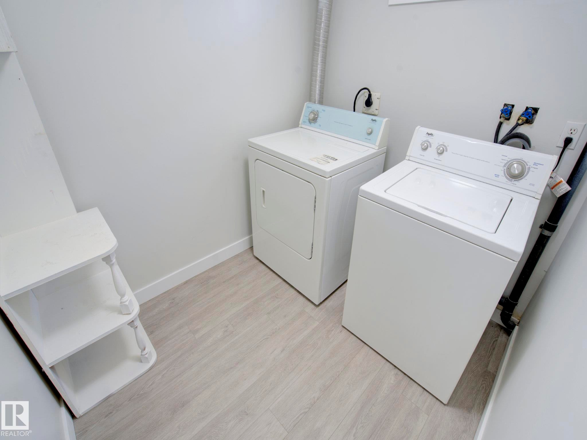 Dedicated laundry area featuring a washer and dryer, light wood-finish flooring, white painted walls, and built-in shelving - 9909 157 Street, Edmonton, AB