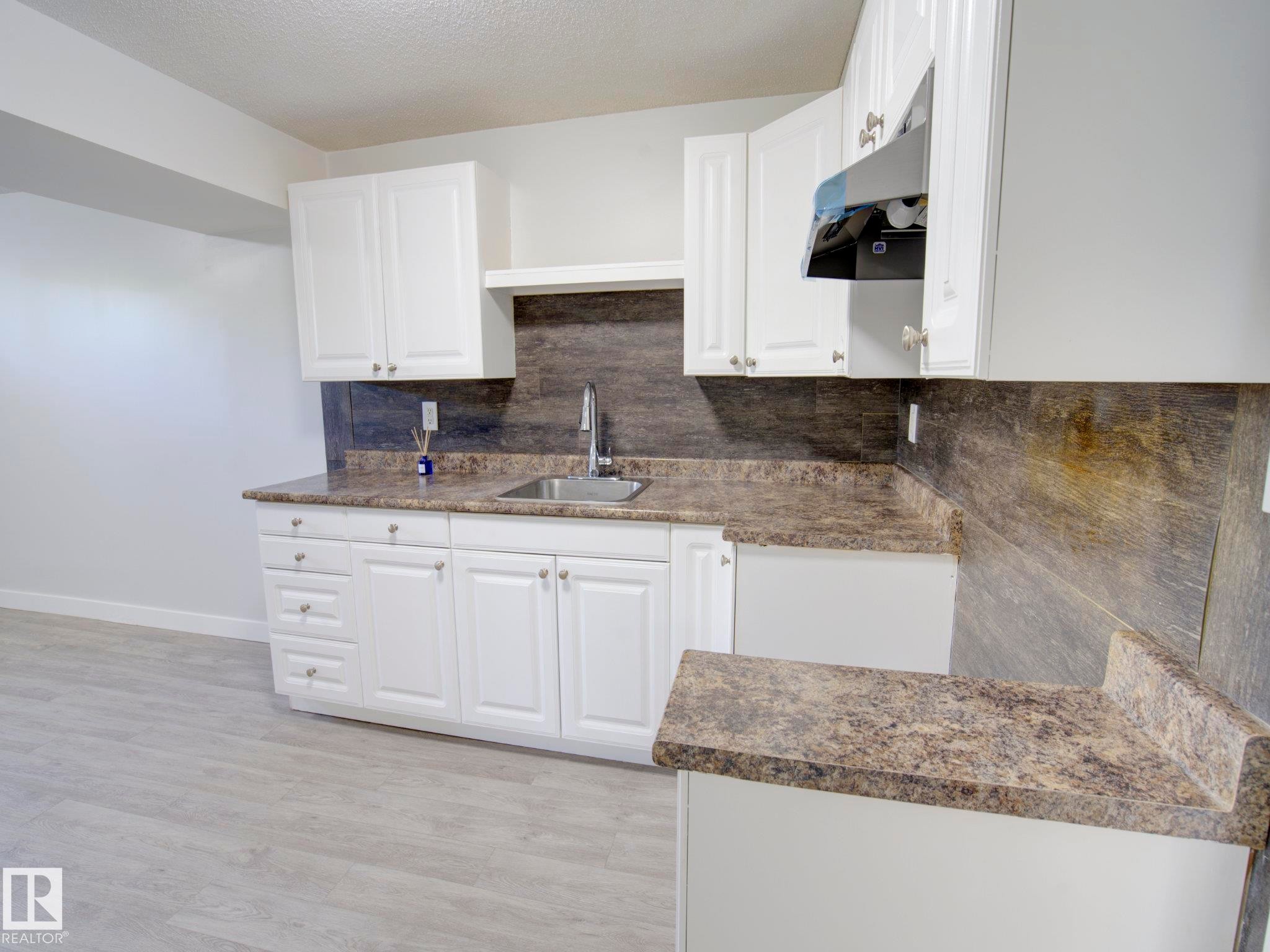 Kitchenette featuring white cabinetry, a stainless steel sink, patterned countertops, and a complementary backsplash - 9909 157 Street, Edmonton, AB