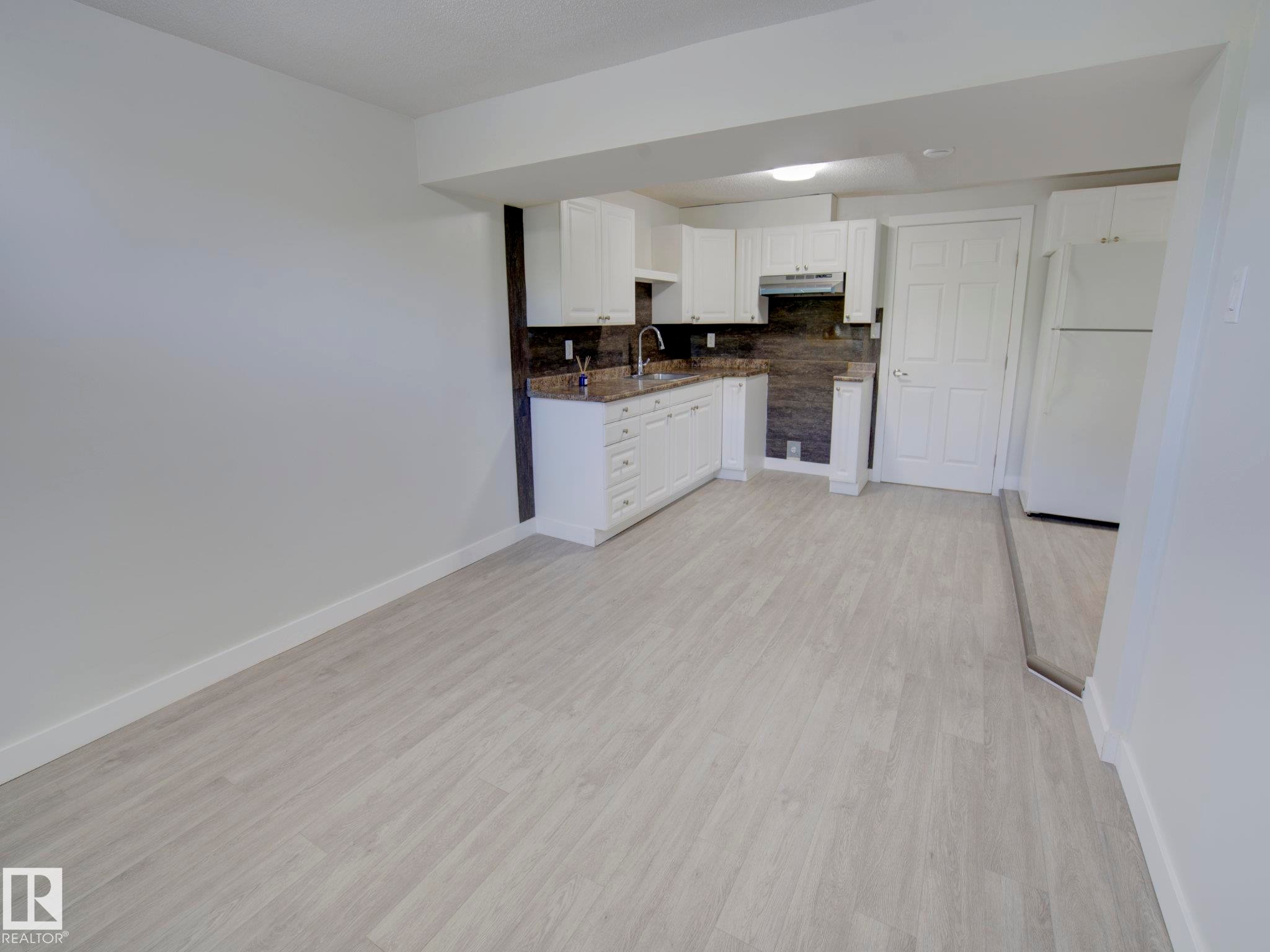 Kitchenette featuring white cabinetry, stone-finish countertops, tile backsplash, and light wood-finish flooring - 9909 157 Street, Edmonton, AB