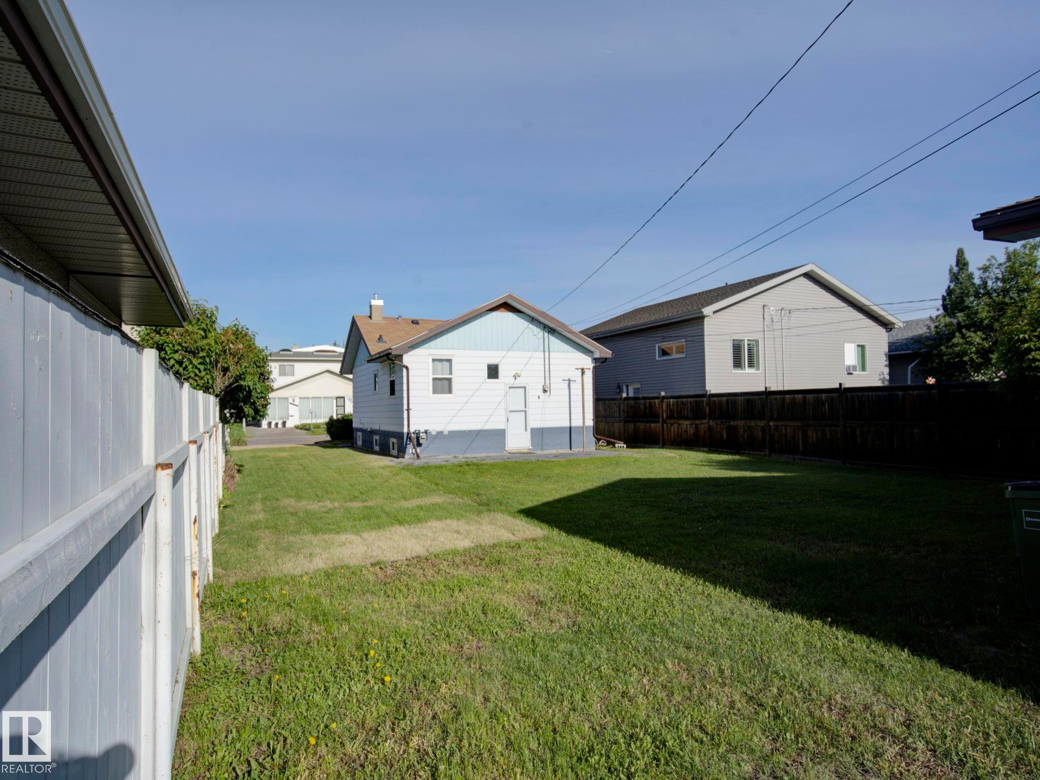 Spacious backyard featuring a large grass area, a partial white privacy fence, and a dark wood privacy fence - 9909 157 Street, Edmonton, AB