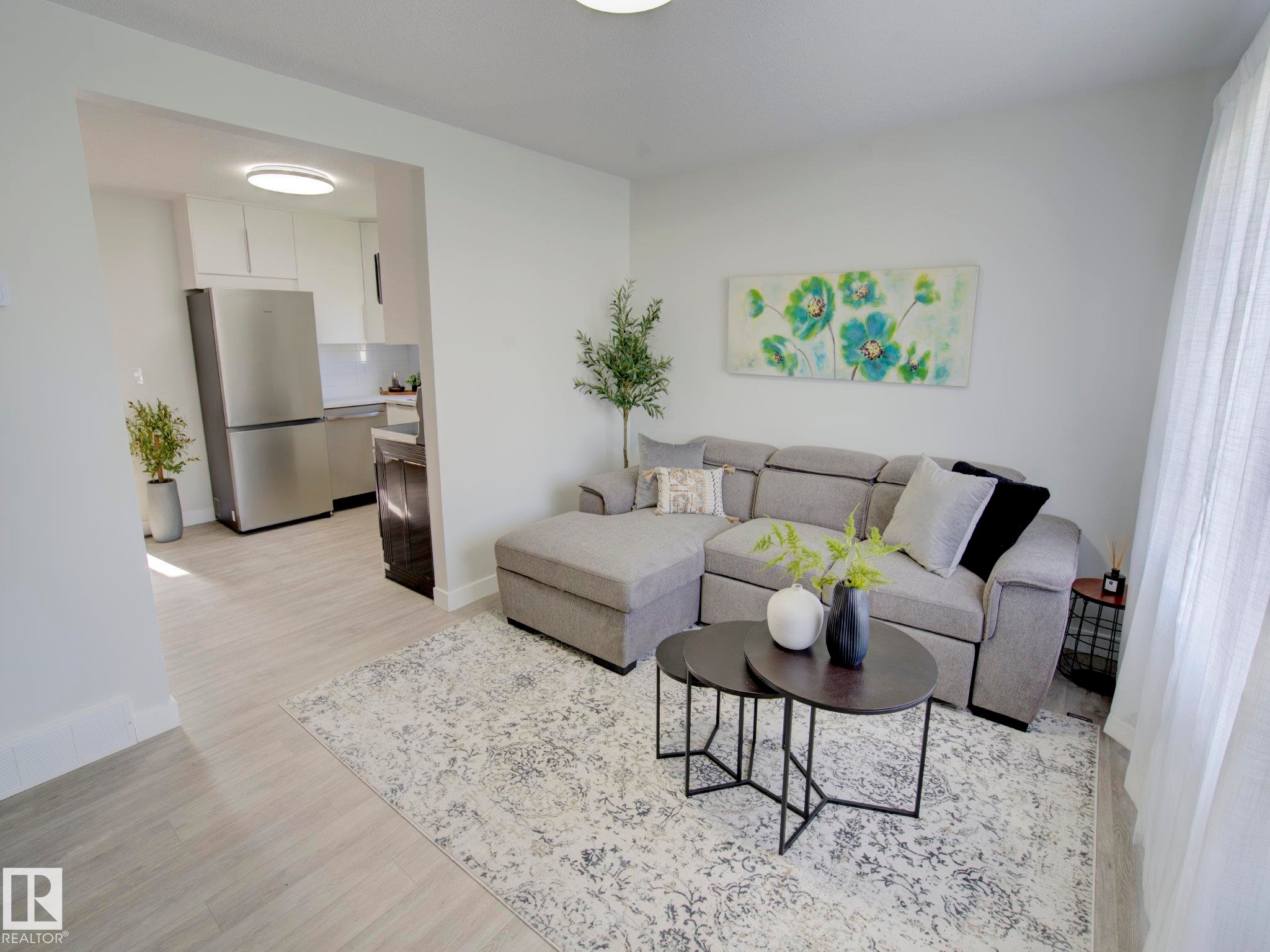 Living area featuring light wood-finish flooring, white walls, and an open entryway to the kitchen - 9909 157 Street, Edmonton, AB