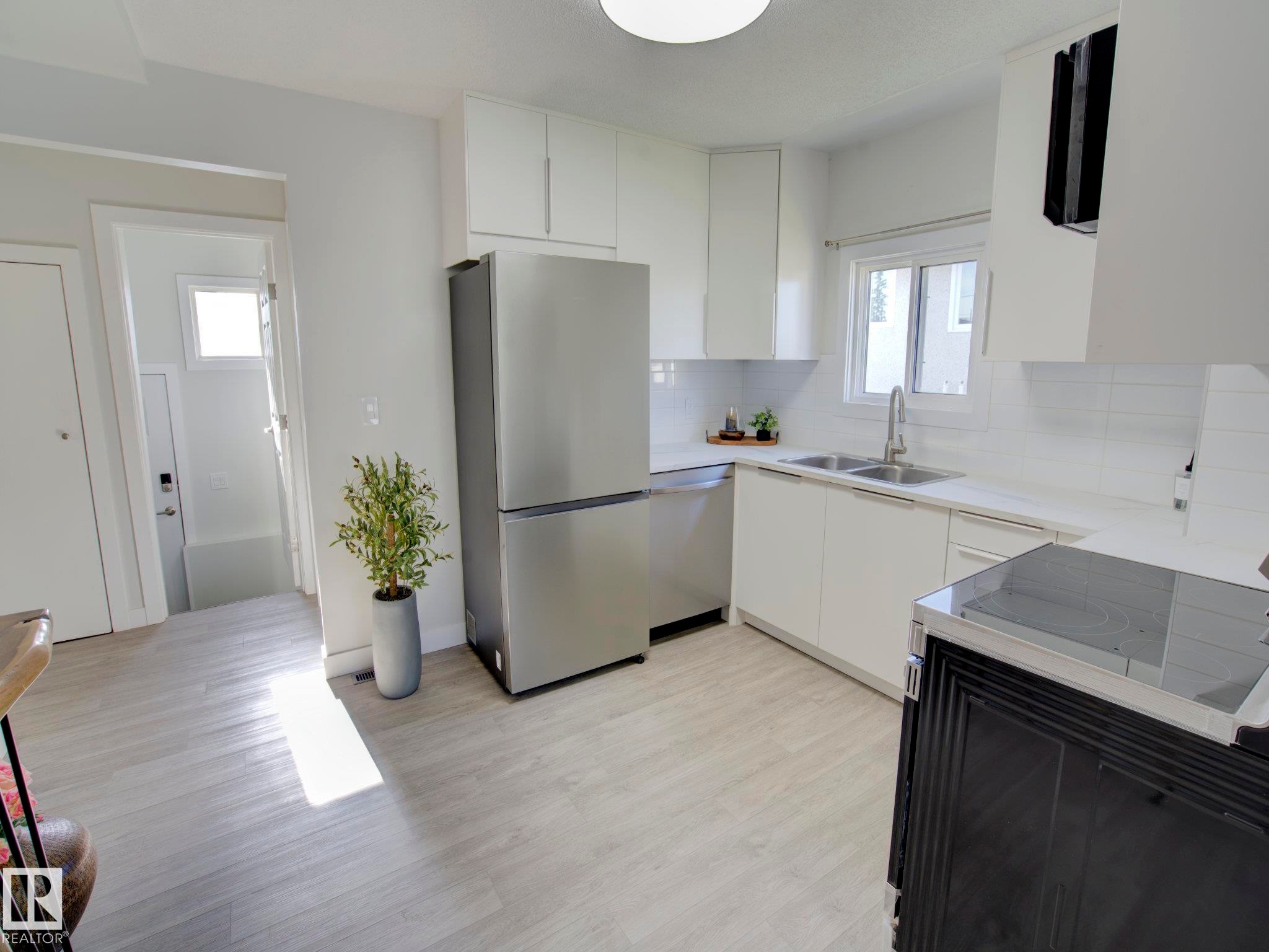 Modern kitchen featuring stainless steel appliances, light wood-finish flooring, white cabinetry, white countertops, and a subway tile backsplash - 9909 157 Street, Edmonton, AB