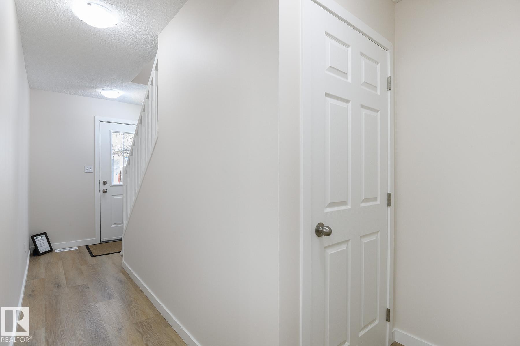Entryway with wood-finish flooring, white paneled interior door, and white painted staircase with balusters - #55 14603 Miller Bv Nw, Edmonton, AB