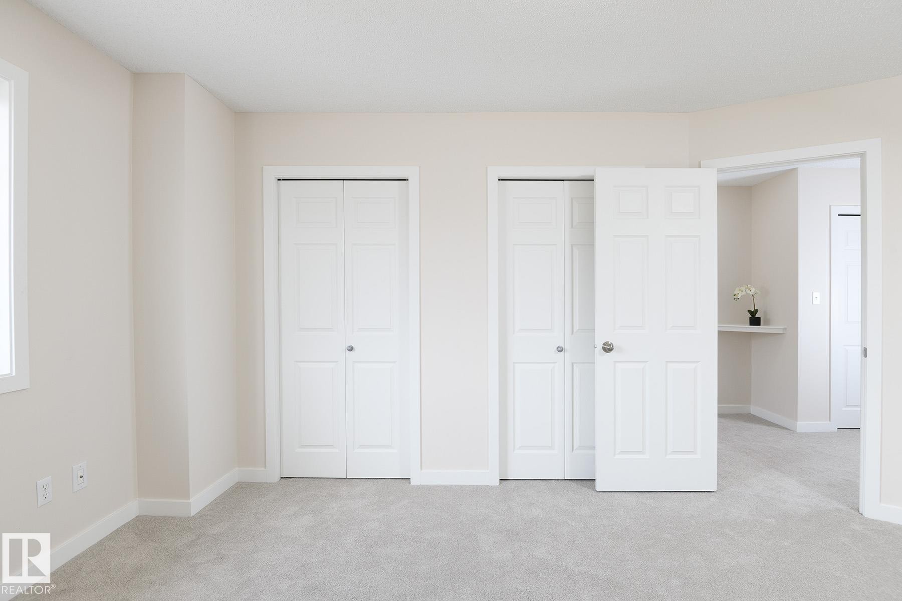 Carpeted interior room featuring two sets of paneled bi-fold closet doors, a white trim window, and neutral wall paint - #55 14603 Miller Bv Nw, Edmonton, AB