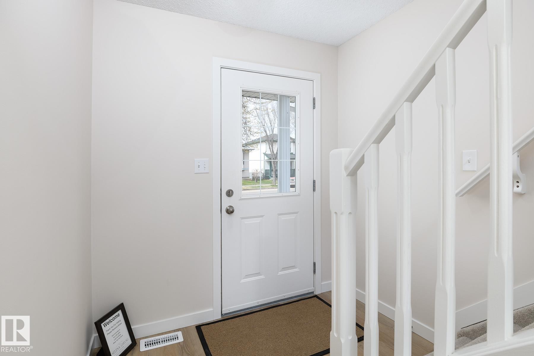 Entryway featuring a white paneled door with a clear glass insert, light-toned walls, and wood-finish flooring - #55 14603 Miller Bv Nw, Edmonton, AB