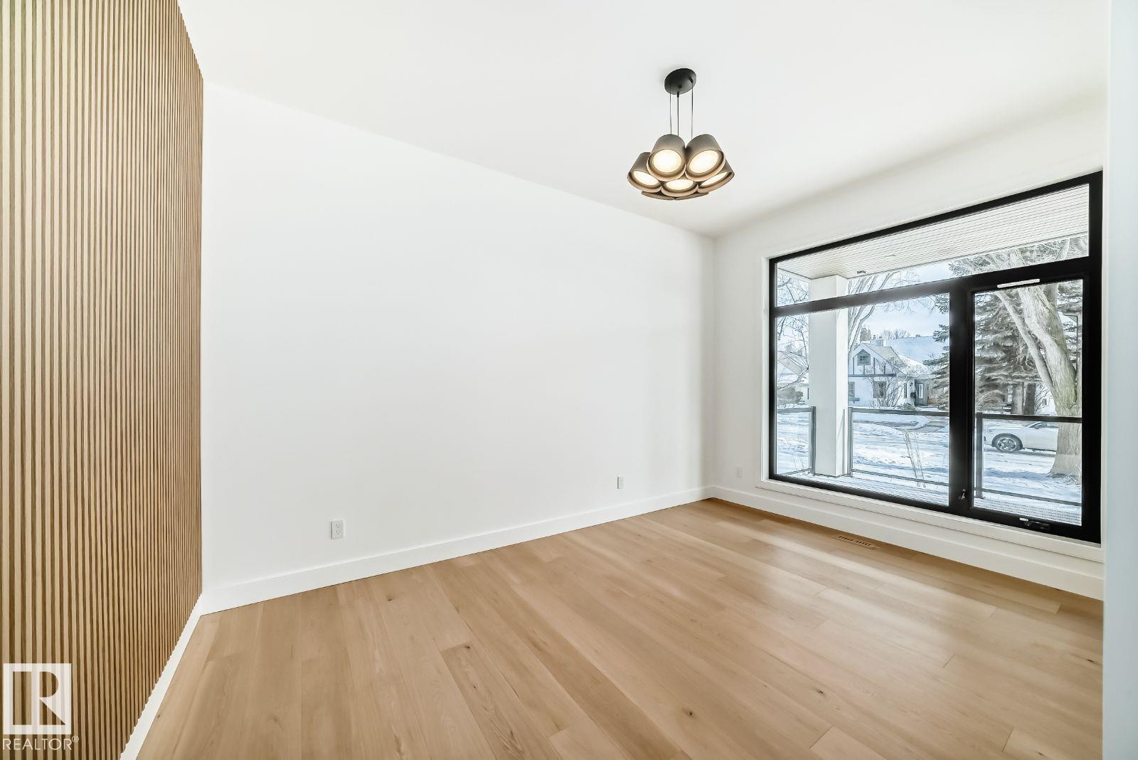 Expansive room featuring wood-finish flooring, a full-height slatted accent wall, and a large black-framed window - 10514 134 Street, Edmonton, AB