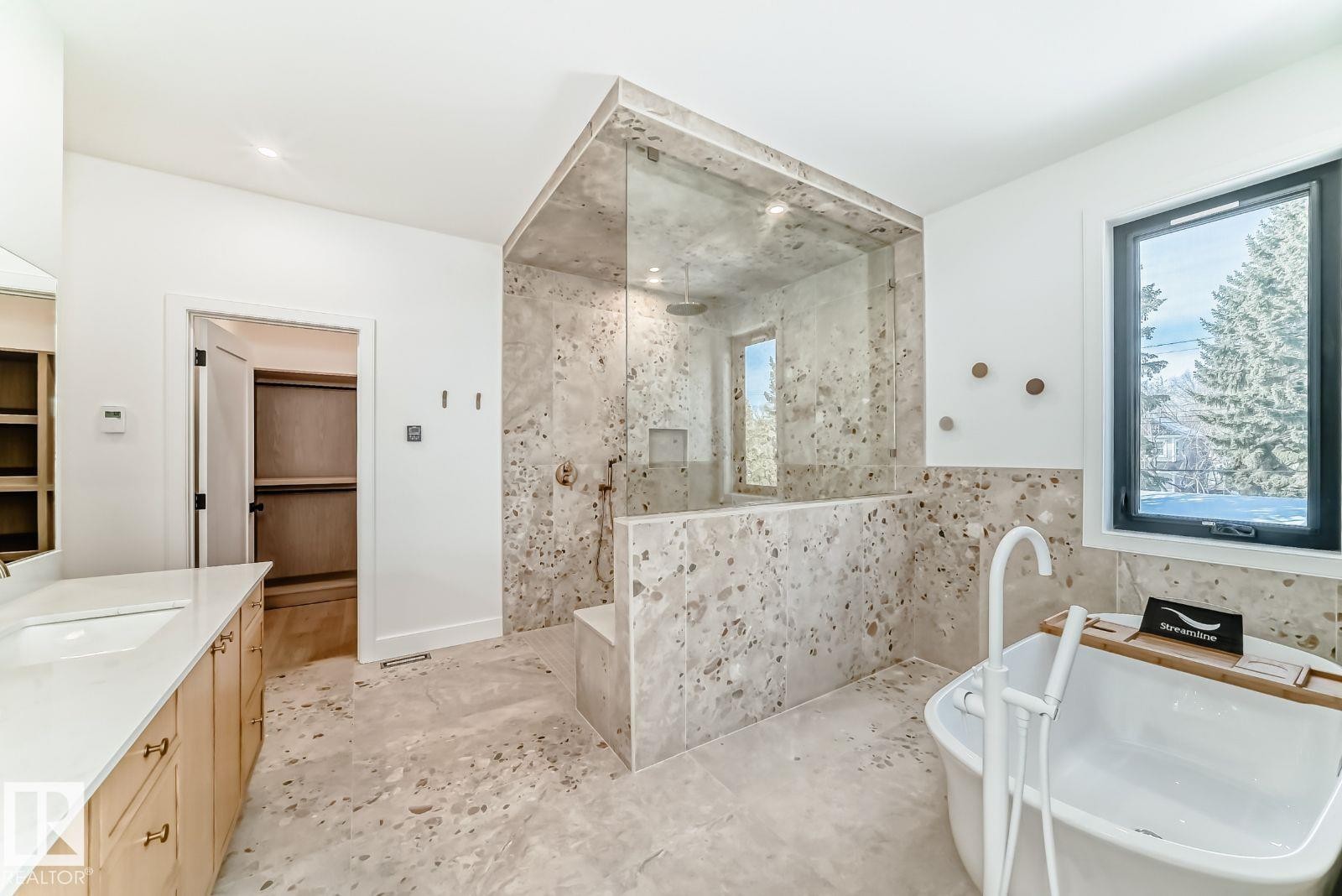 Spacious bathroom featuring a freestanding soaking tub, a glass-enclosed shower with a built-in bench, dual vanity with undermount sinks, and light-toned wood-finish cabinetry - 10514 134 Street, Edmonton, AB