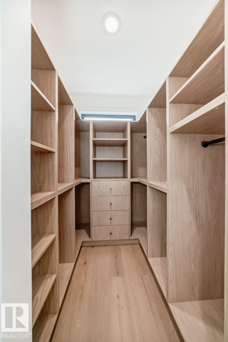 Custom closet system featuring natural wood-finish shelving, built-in drawers with brass hardware, dedicated hanging rods, and recessed ceiling lighting - 10514 134 Street, Edmonton, AB