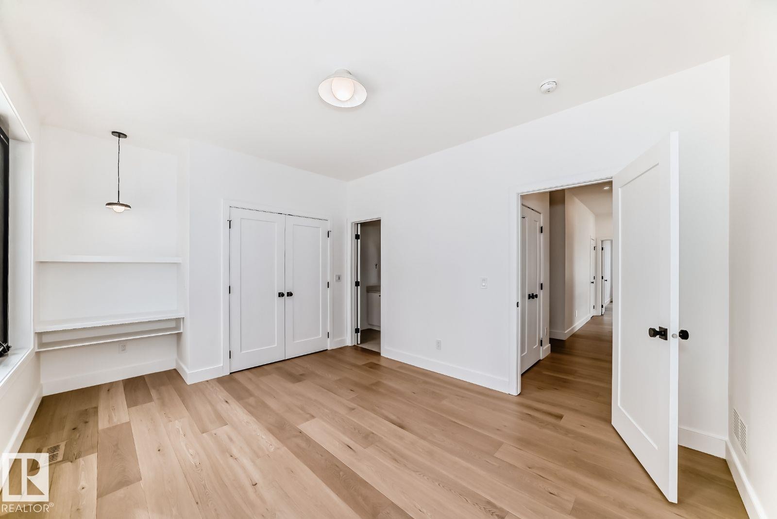 Bright room featuring wide plank wood-finish flooring, a built-in desk with shelving, a contemporary pendant light fixture, and a flush-mount ceiling light - 10514 134 Street, Edmonton, AB