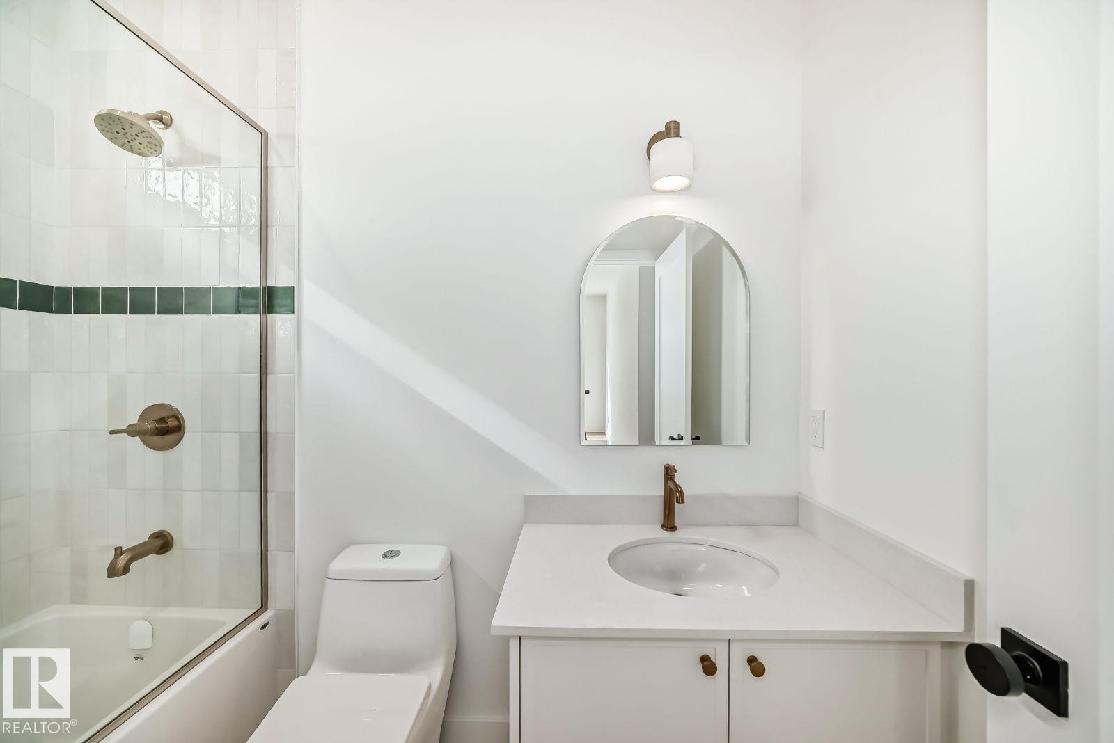 Bathroom featuring a white subway tile shower surround with a green accent band, a glass shower enclosure, and bronze-finish fixtures - 10514 134 Street, Edmonton, AB