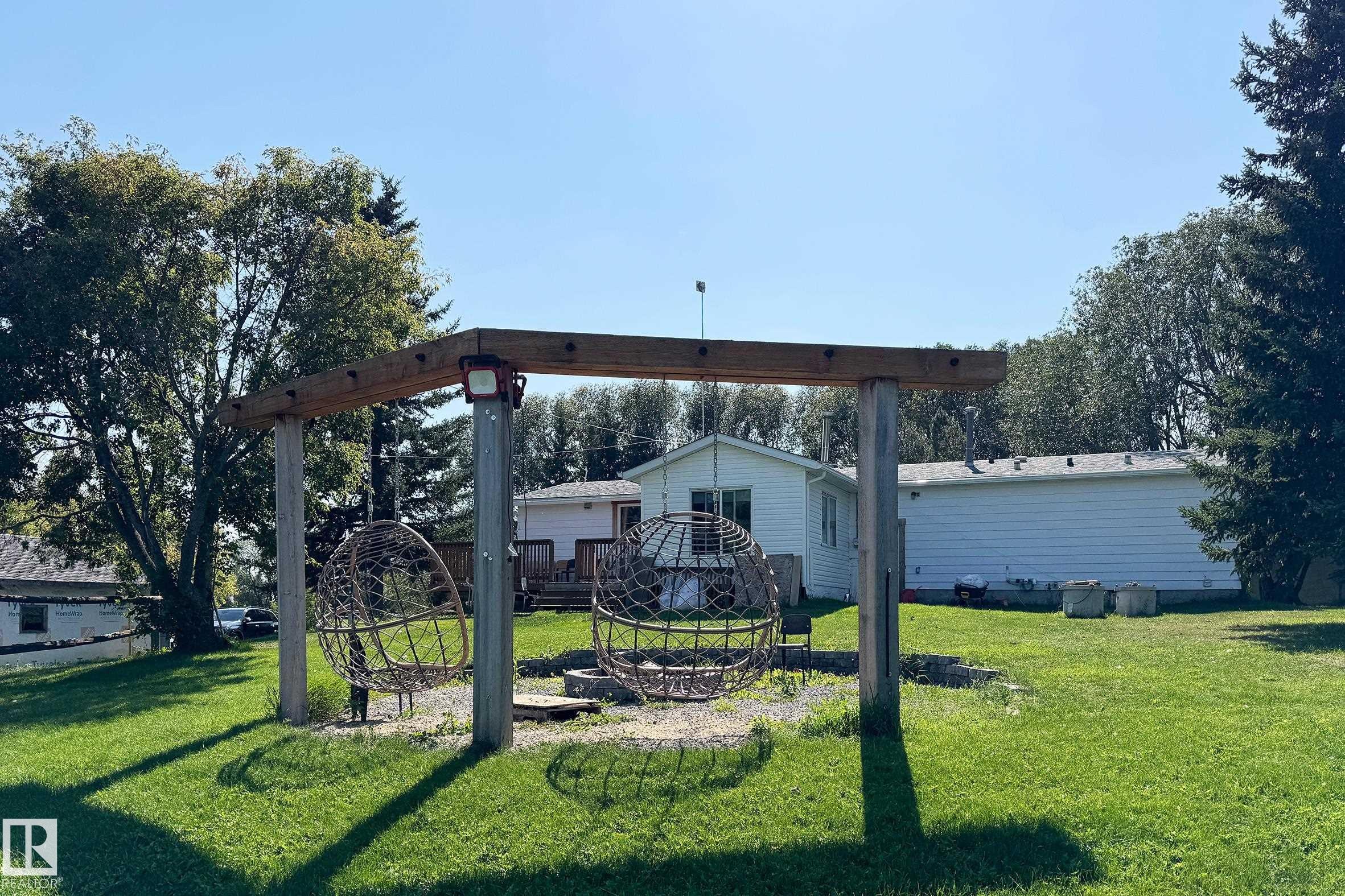 Outdoor entertaining area featuring a wooden pergola structure, two suspended sphere chairs, and a gravel fire pit area - 3054 28 Avenue, Edmonton, AB