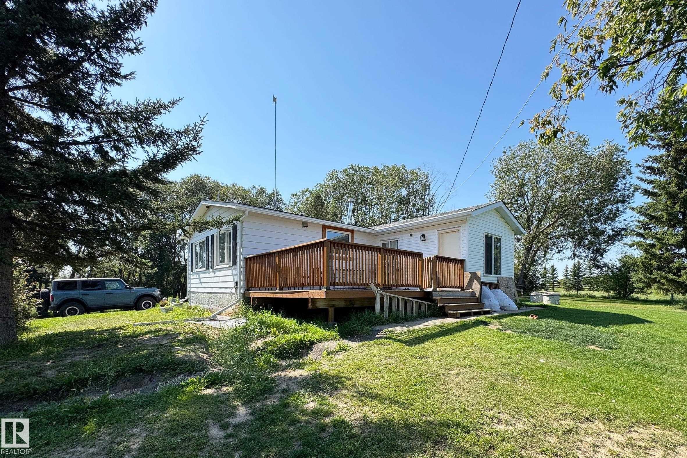 White siding residence featuring a spacious wooden deck with railings, an accessibility ramp, and stairs - 3054 28 Avenue, Edmonton, AB