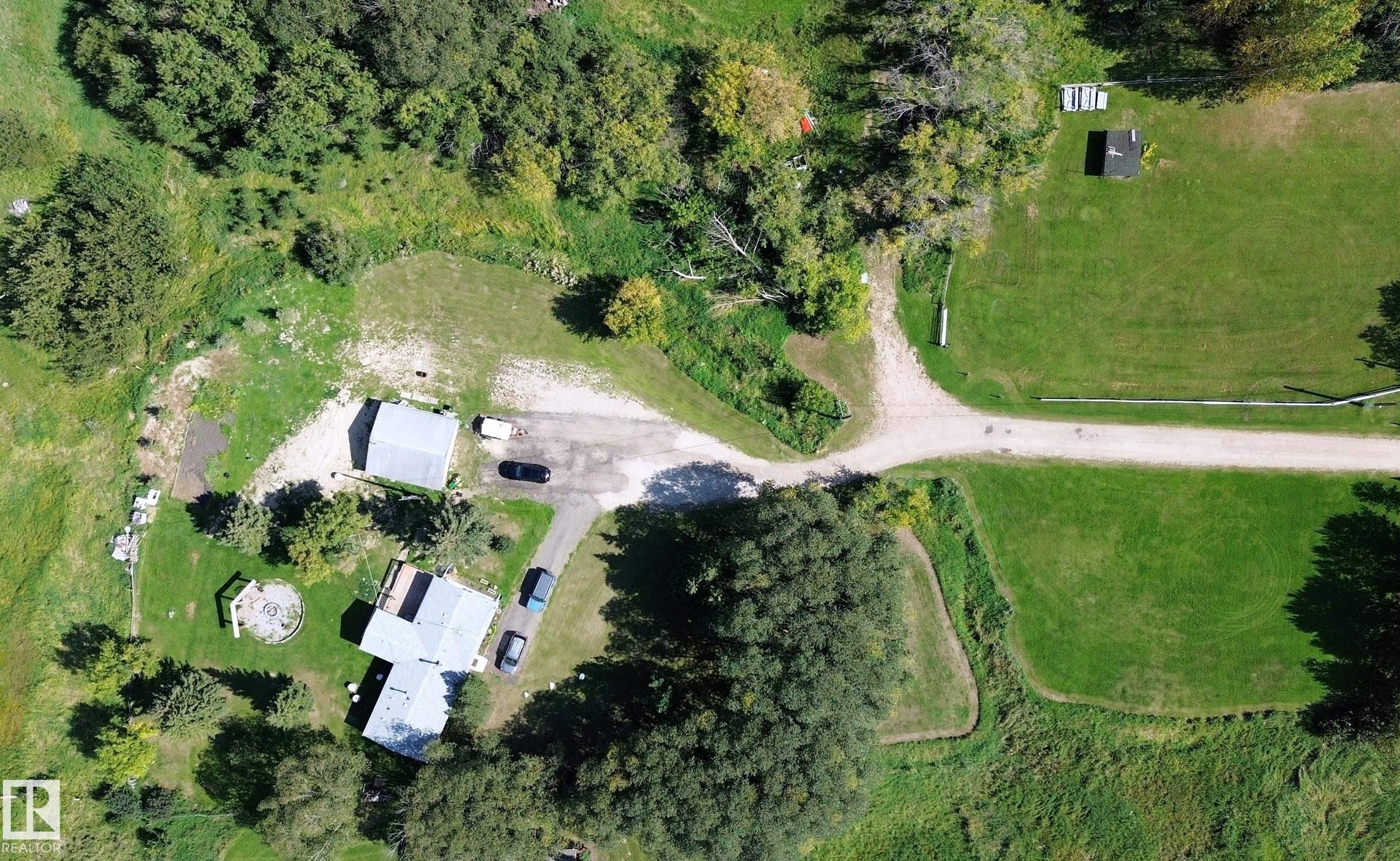 Expansive property featuring a gravel driveway, multiple structures with light-colored roofing, a manicured lawn, and mature trees - 3054 28 Avenue, Edmonton, AB