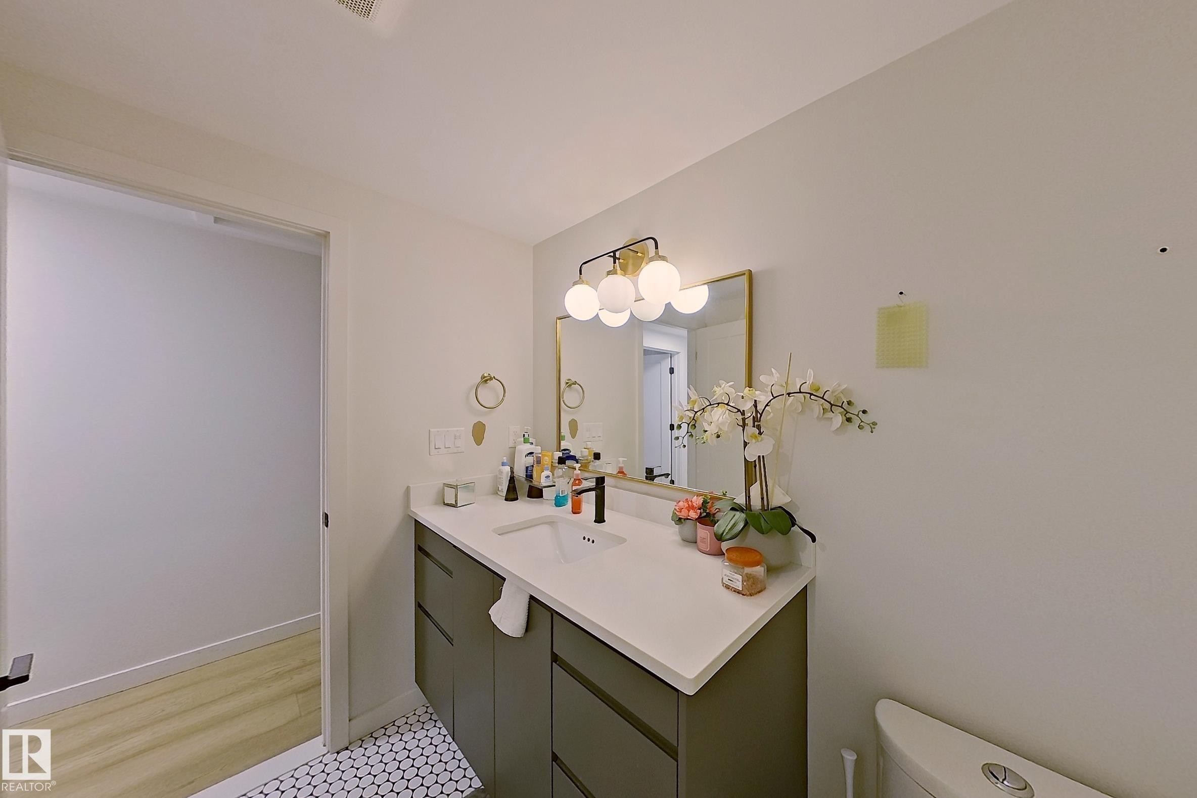 Bathroom featuring a contemporary vanity with a white countertop and integrated sink, a gold-framed mirror, and a modern light fixture with spherical globes - 3054 28 Avenue, Edmonton, AB