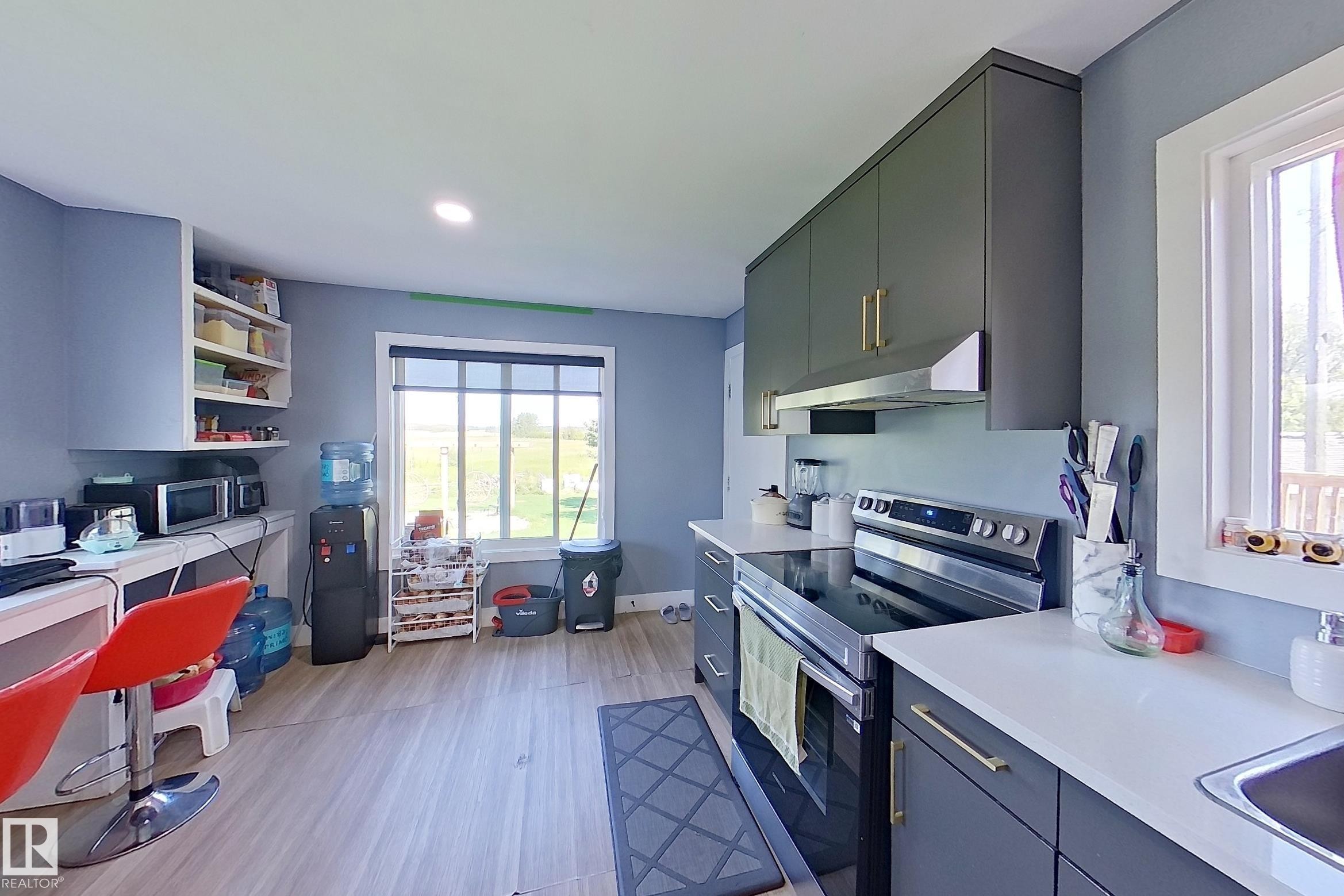 Kitchen featuring wood-finish flooring, dark grey cabinetry with gold-tone hardware, white countertops, built-in shelving, and a stainless steel range with overhead ventilation - 3054 28 Avenue, Edmonton, AB