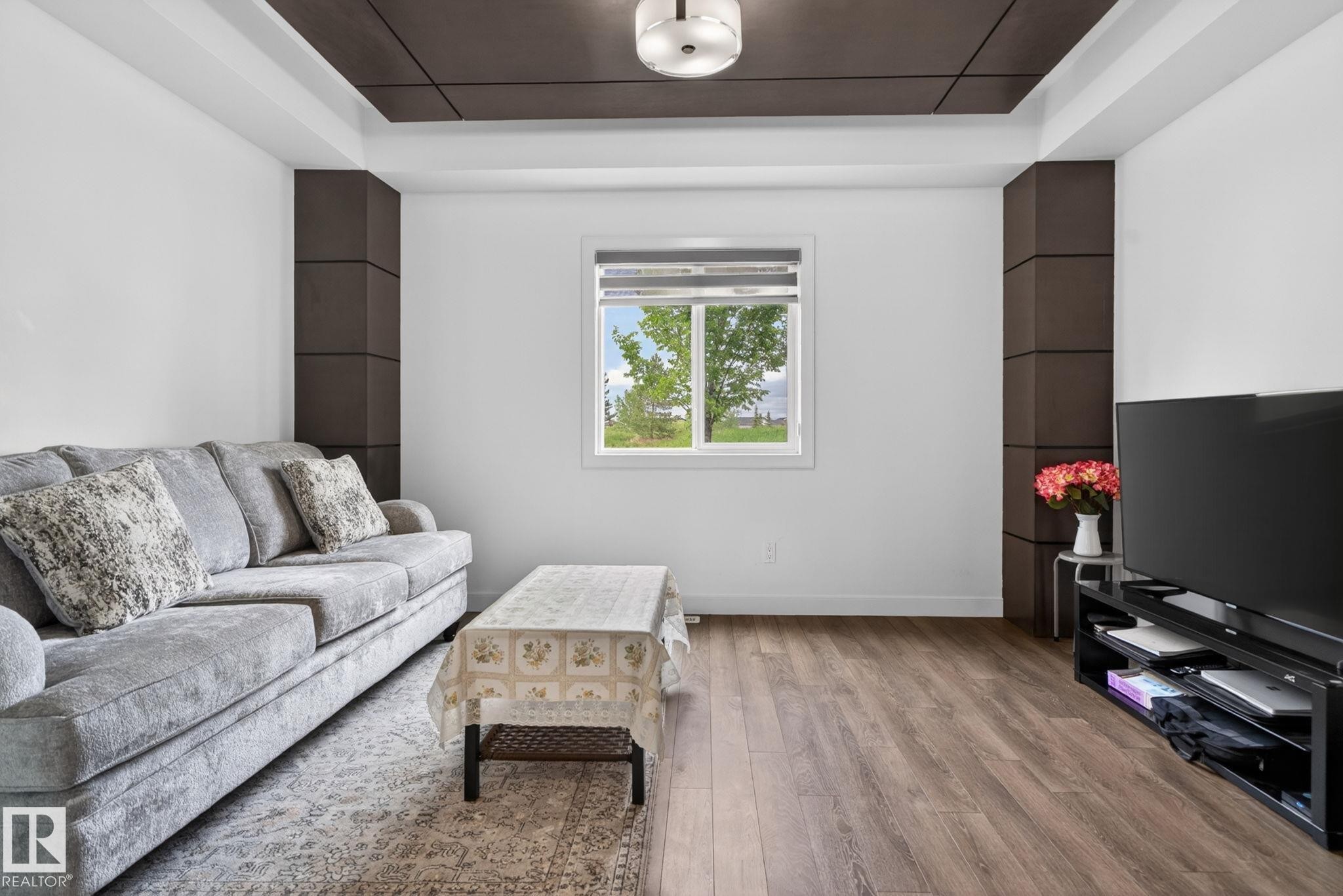 Living area featuring wood-finish flooring, a contemporary overhead light fixture, and a window with exterior views - 704 39 Street, Edmonton, AB