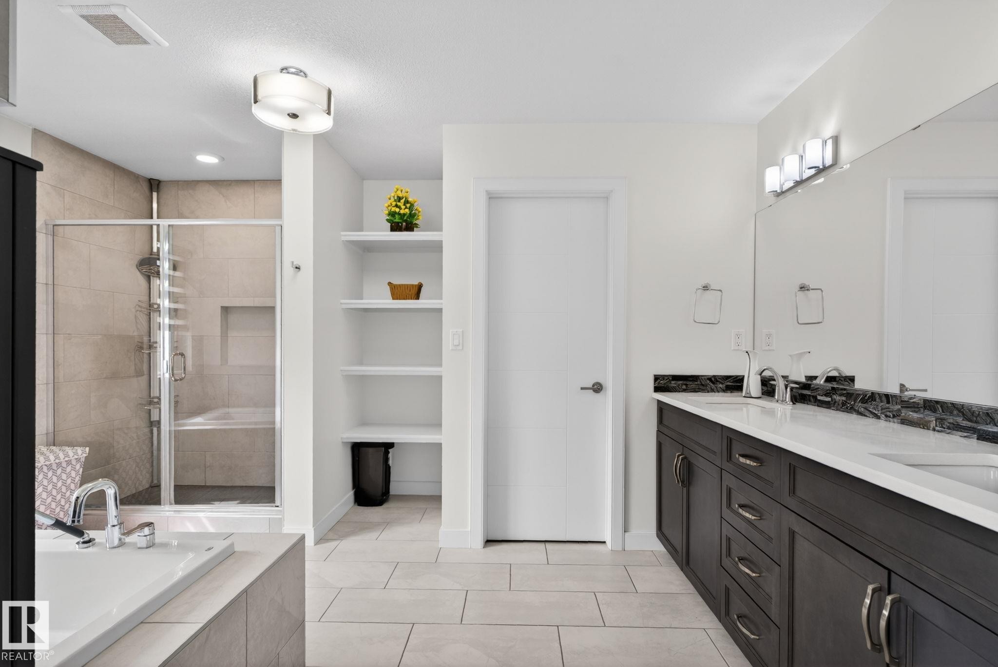 Spacious bathroom featuring a dual vanity with dark wood cabinetry and white countertops, a glass-enclosed shower with tile surround, an adjacent built-in soaking tub, and open shelving - 704 39 Street, Edmonton, AB