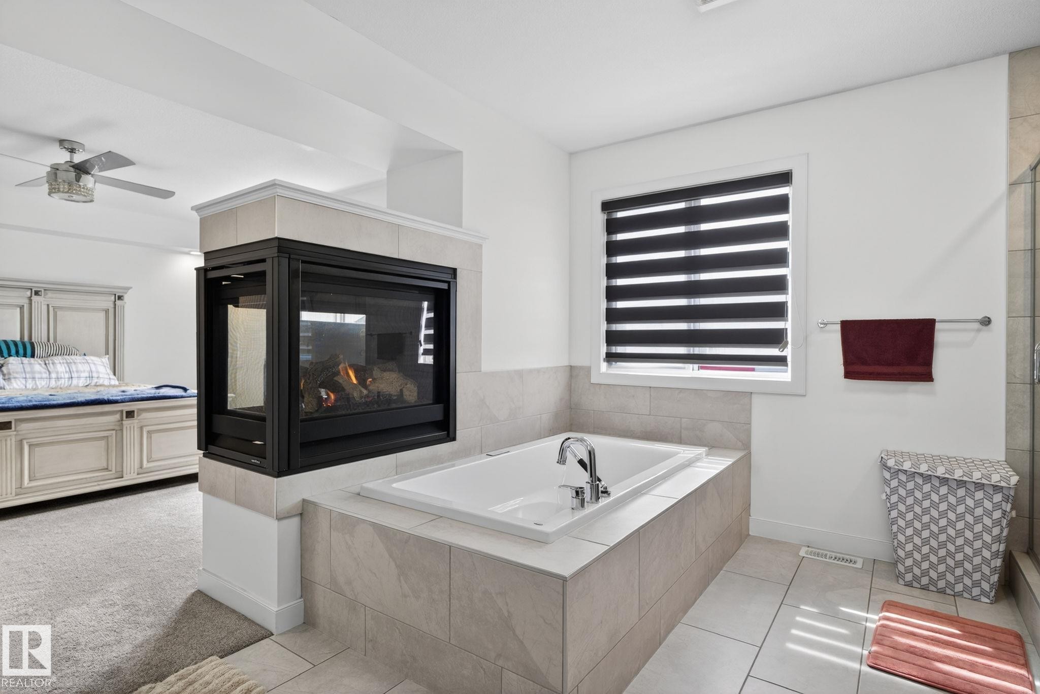 Two-sided fireplace featuring a tiled surround and an inset soaking tub with deck-mounted fixtures - 704 39 Street, Edmonton, AB