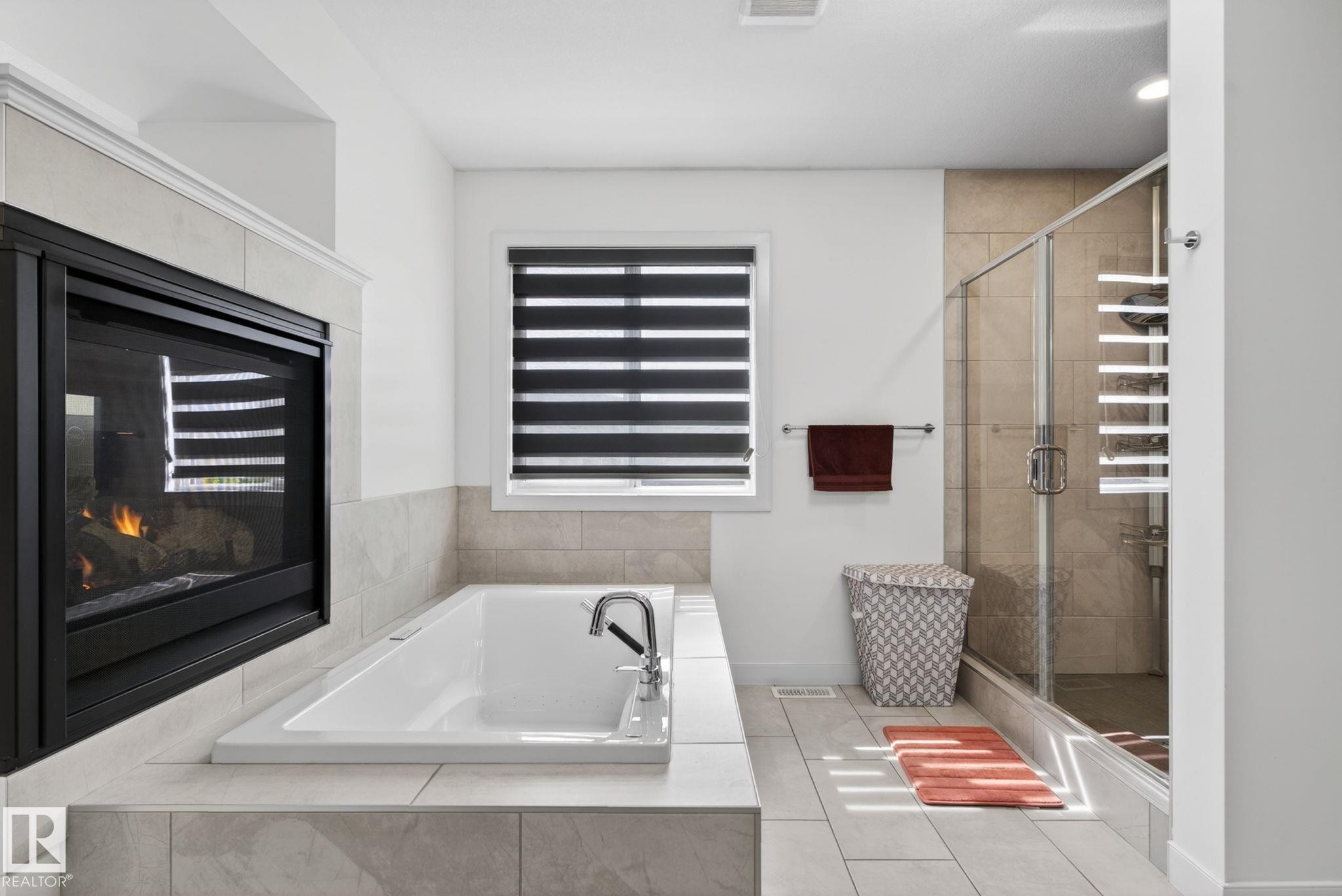 Integrated fireplace with a tile surround, a built-in soaking tub with deck-mounted fixtures, a glass-enclosed shower, and large format floor tiling - 704 39 Street, Edmonton, AB