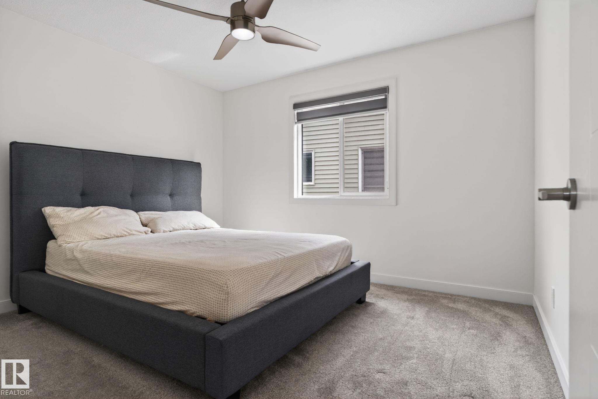 Carpeted room featuring a ceiling fan with integrated lighting, white walls, and a window with a roller shade - 704 39 Street, Edmonton, AB