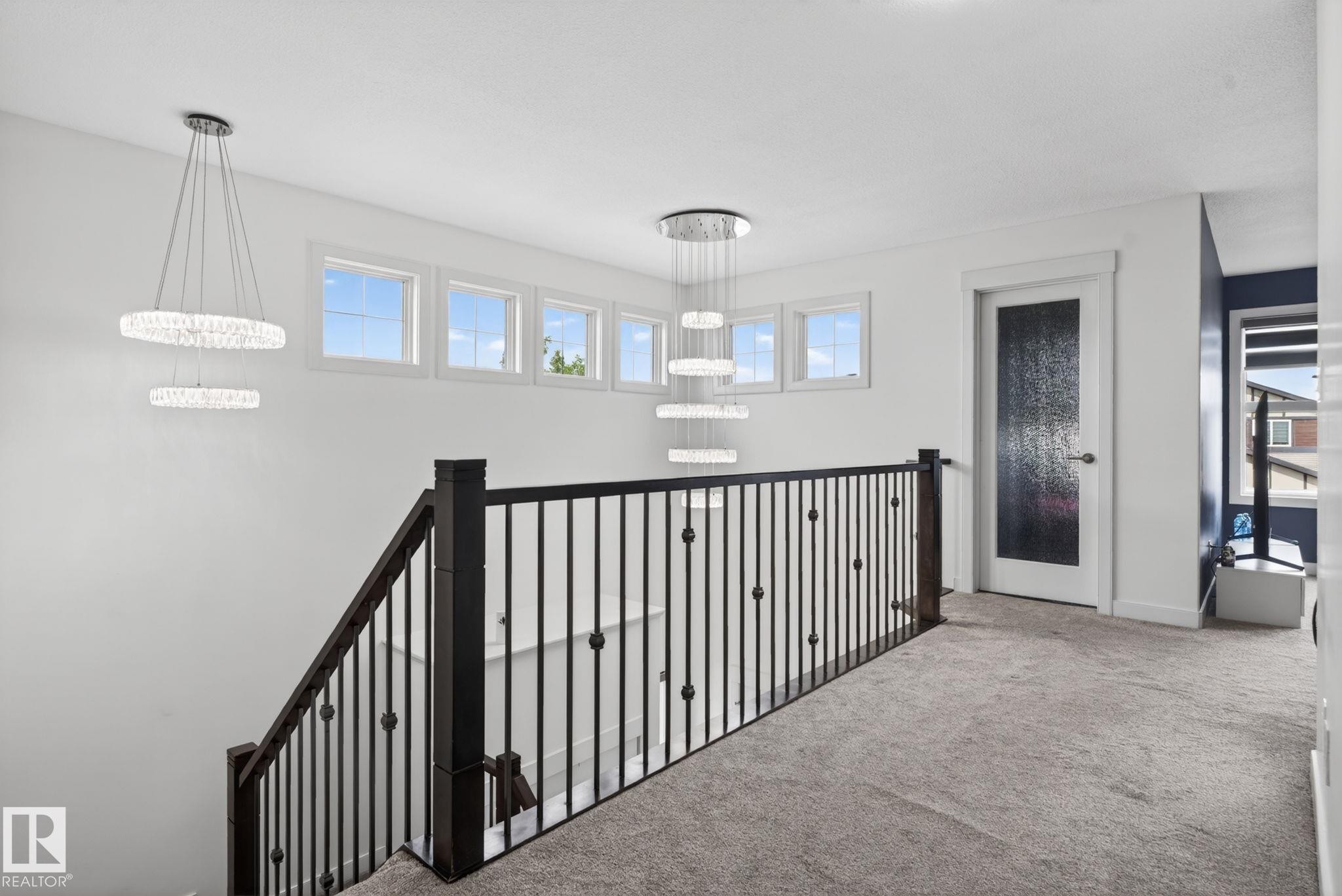 Upper-level landing featuring a dark wood and wrought iron staircase railing, multiple transom windows, and two tiered crystal chandeliers - 704 39 Street, Edmonton, AB