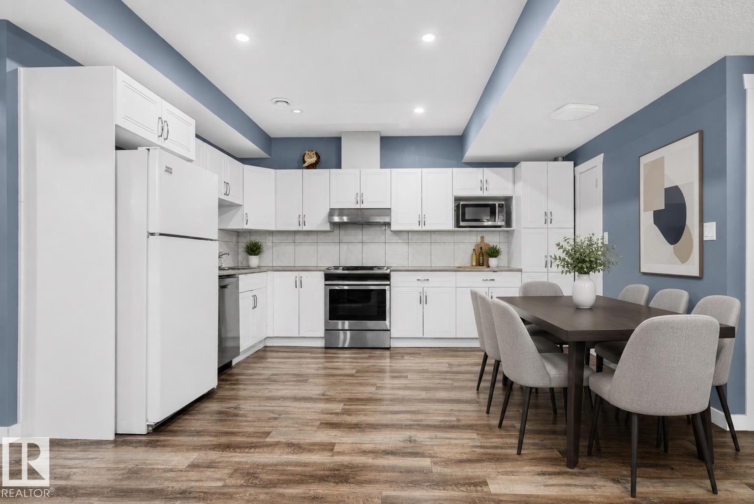 Open-concept kitchen and dining area featuring wood-finish flooring, white cabinetry, integrated stainless steel appliances, and recessed lighting - 704 39 Street, Edmonton, AB