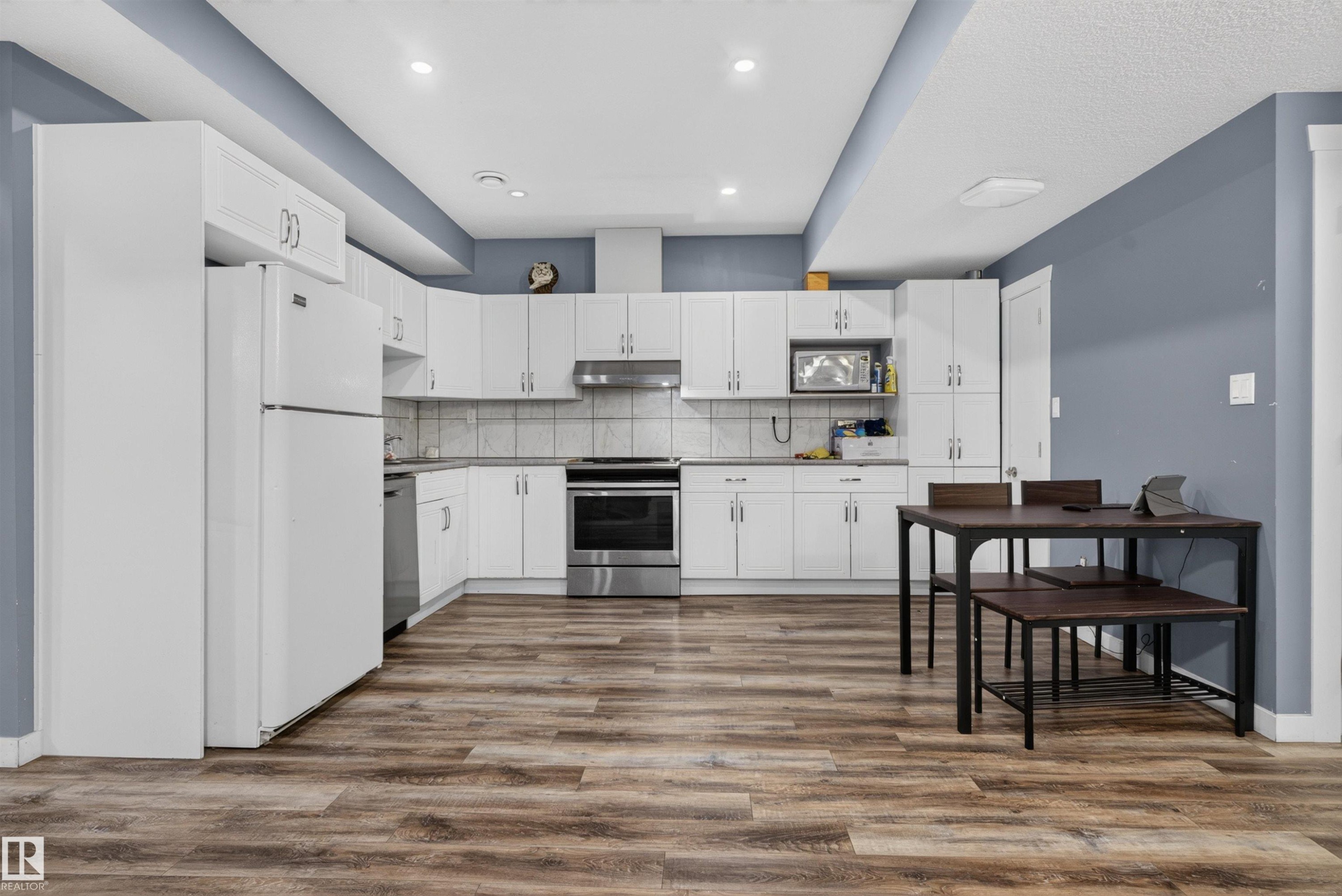 Kitchen featuring white cabinetry, wood-finish flooring, stainless steel appliances, recessed lighting, and a neutral tile backsplash - 704 39 Street, Edmonton, AB