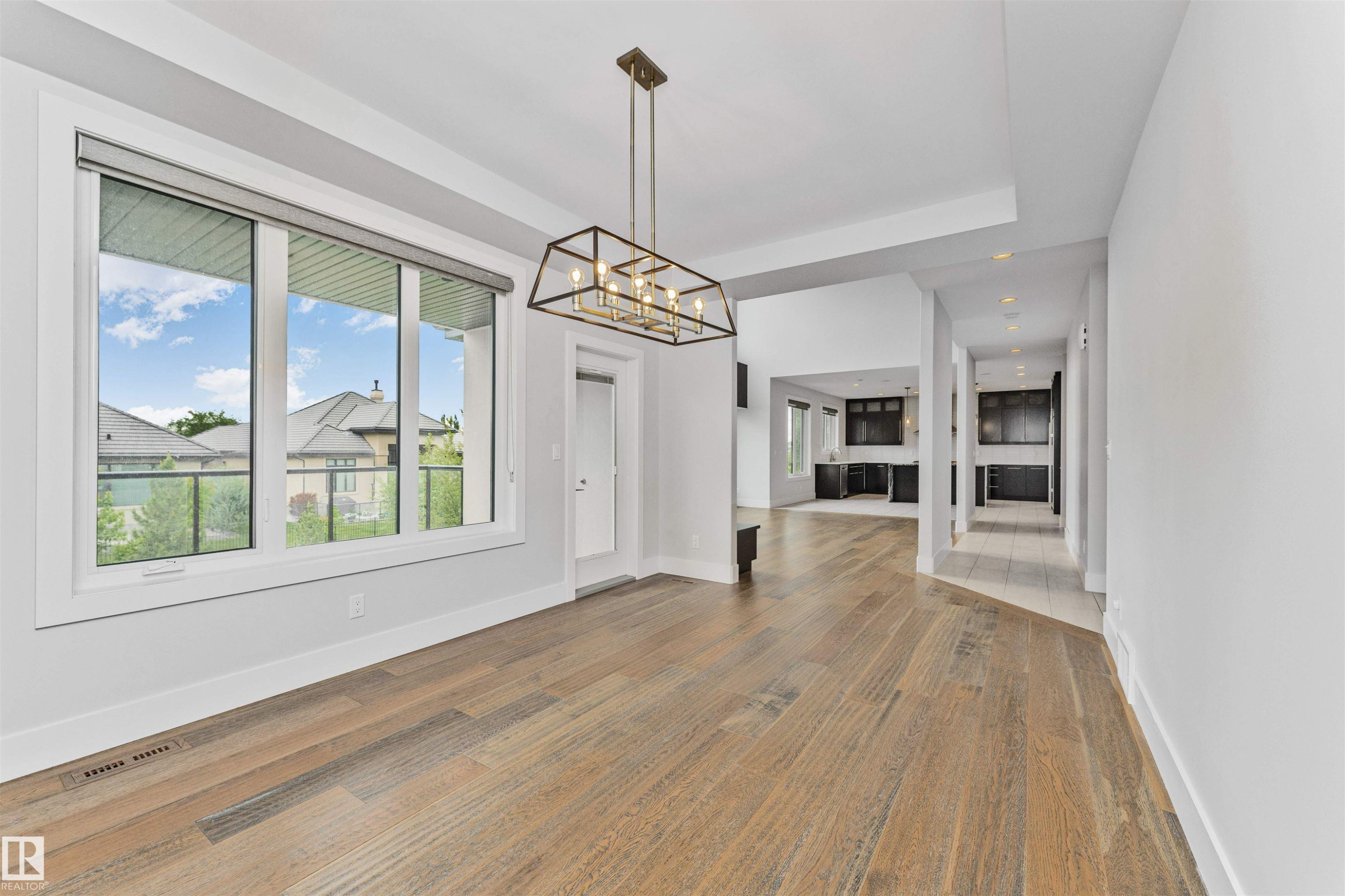 Spacious interior featuring wide-plank wood-finish flooring, a modern linear chandelier, and expansive windows - 3310 Watson Bay, Edmonton, AB