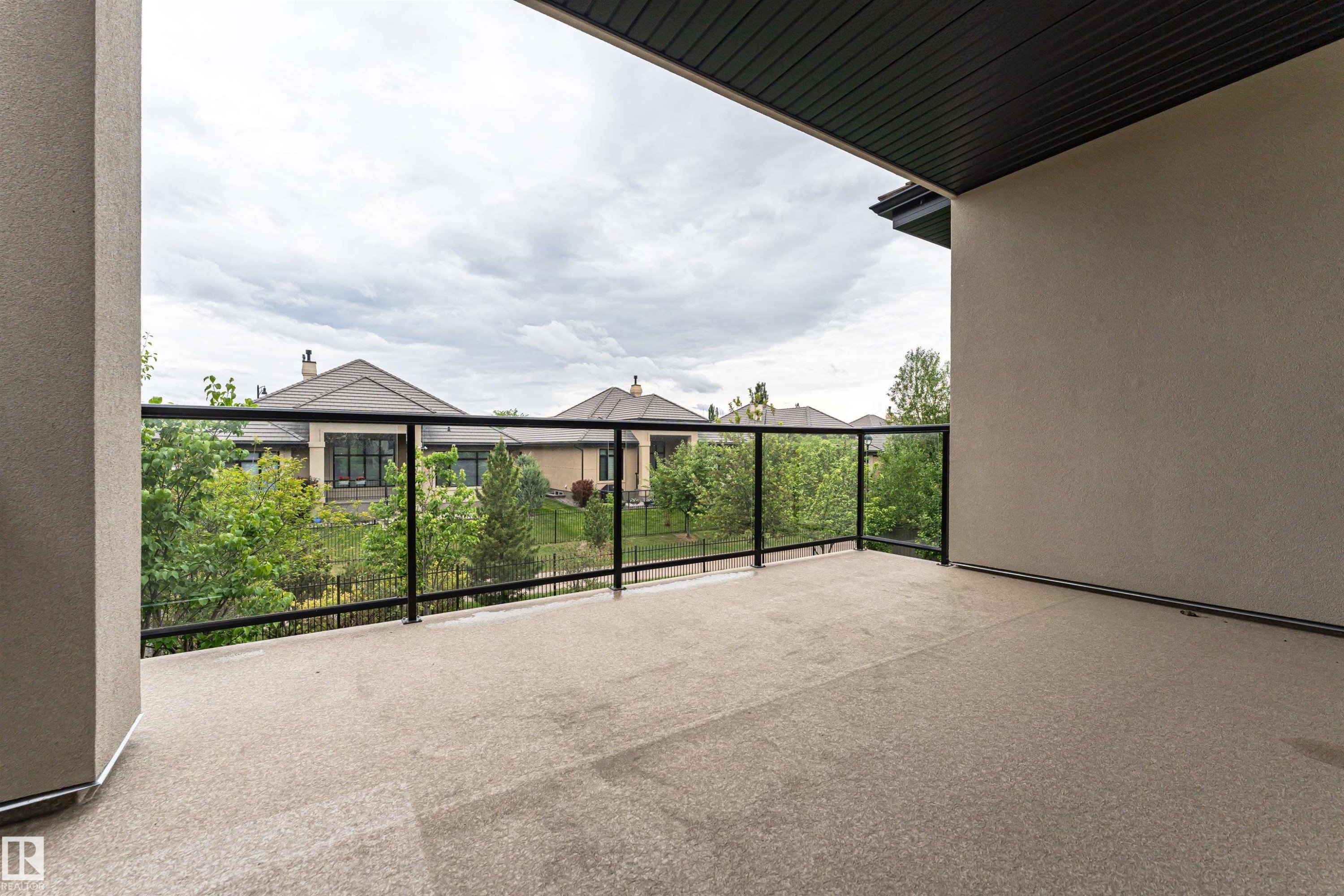 Outdoor balcony featuring a textured concrete floor, clear glass railings with black metal framing, and a stucco exterior wall - 3310 Watson Bay, Edmonton, AB