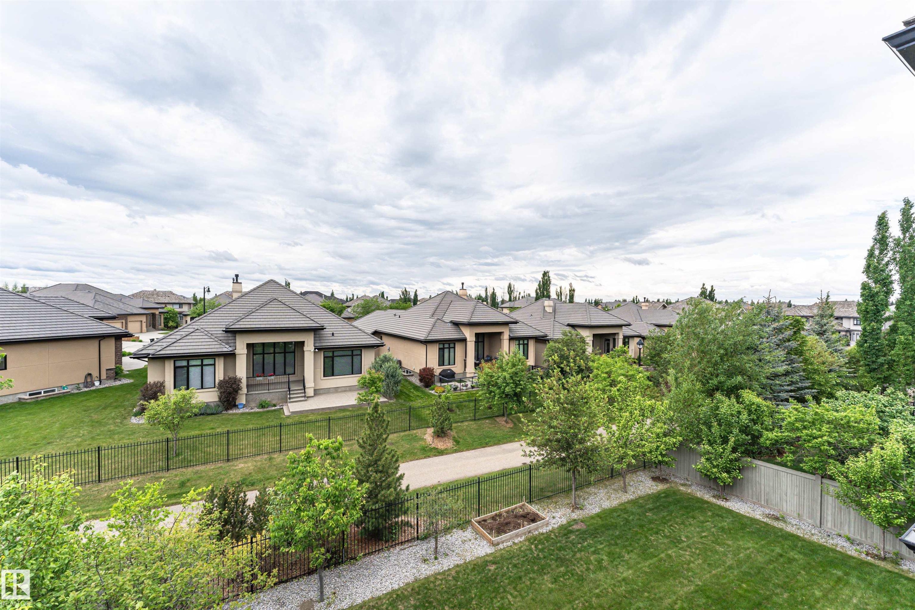 Rear exterior featuring a manicured lawn, dark metal fencing, and mature landscaping - 3310 Watson Bay, Edmonton, AB