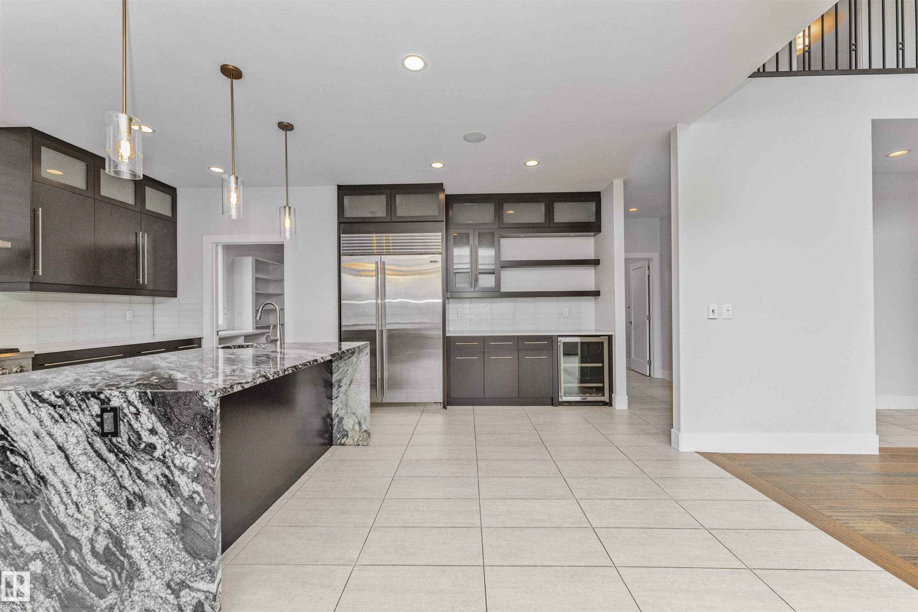 Gourmet kitchen featuring a large island with a waterfall edge, dark wood-finish cabinetry, stainless steel appliances, a beverage cooler, and pendant lighting - 3310 Watson Bay, Edmonton, AB