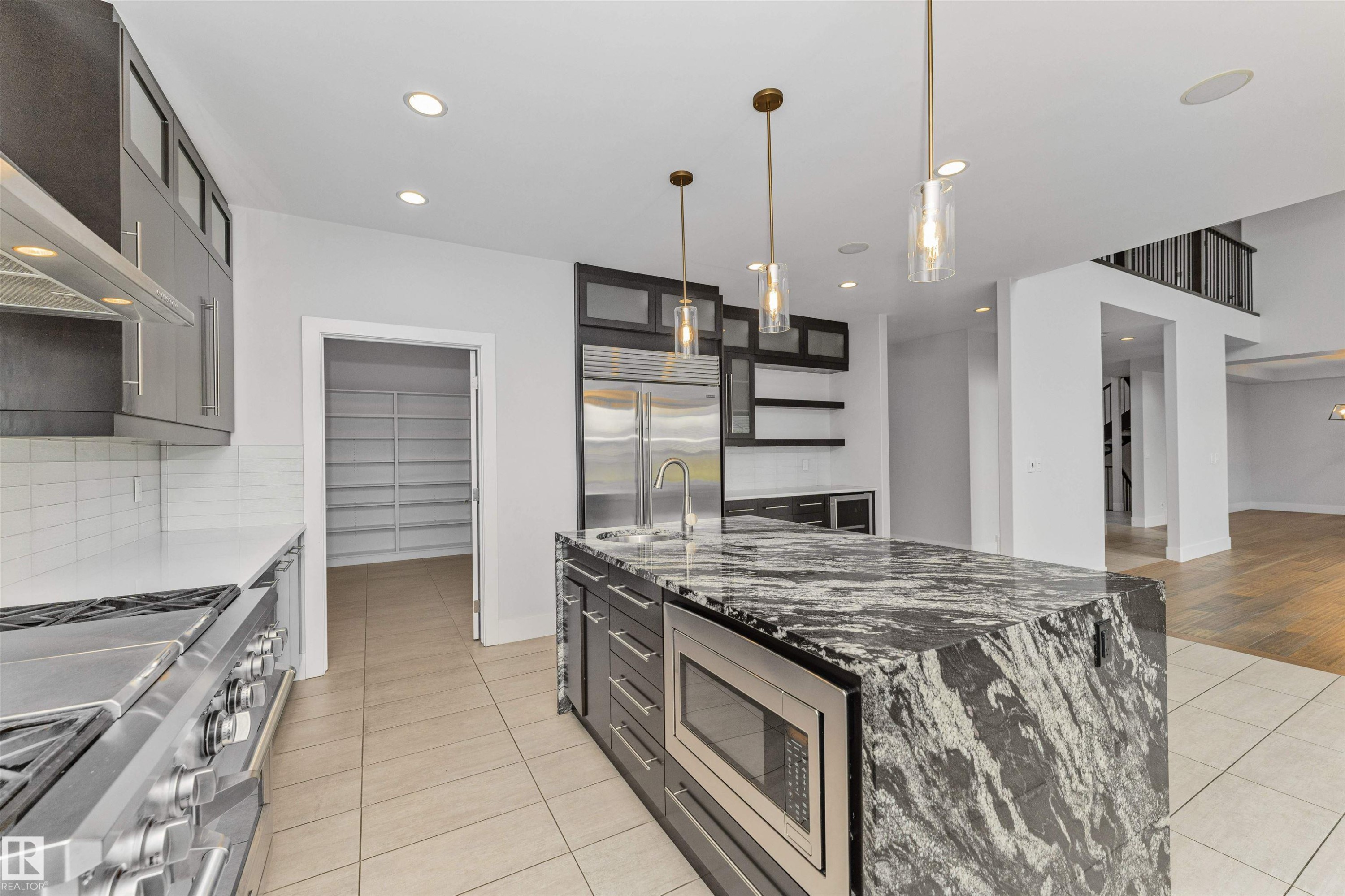 Kitchen featuring a large waterfall island with integrated microwave, stainless steel appliances, contemporary pendant lighting, and a walk-in pantry with extensive shelving - 3310 Watson Bay, Edmonton, AB