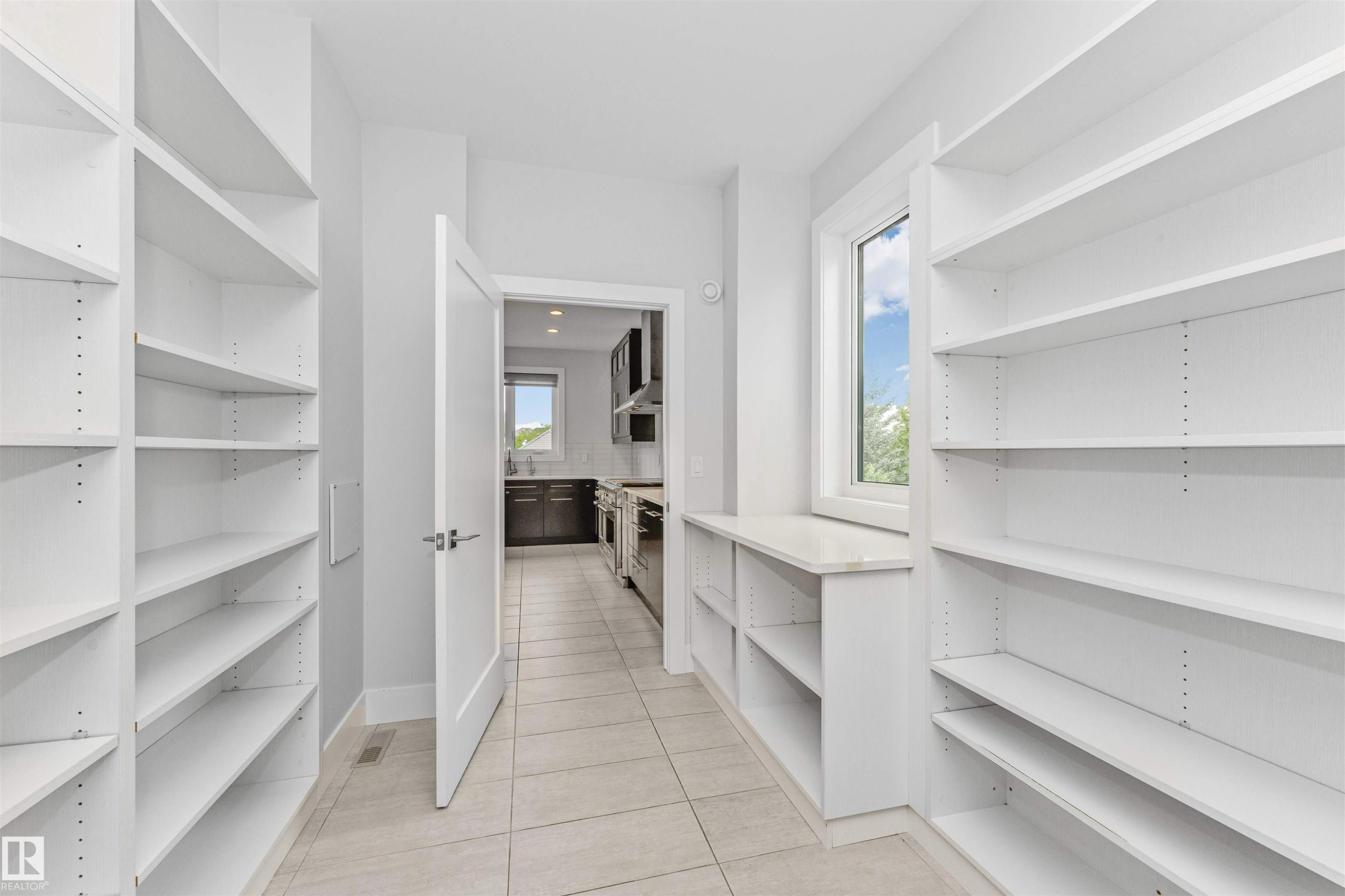 Spacious pantry featuring extensive built-in shelving, tile flooring, a window providing natural light, and a built-in countertop surface - 3310 Watson Bay, Edmonton, AB