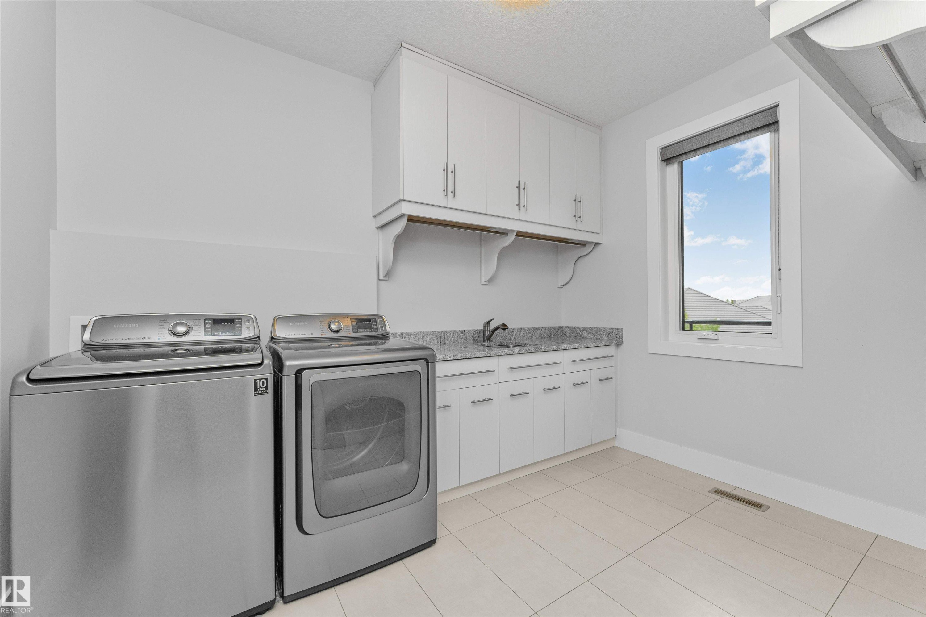 Functional laundry room featuring a utility sink, white cabinetry with silver hardware, and a light-toned tile floor - 3310 Watson Bay, Edmonton, AB