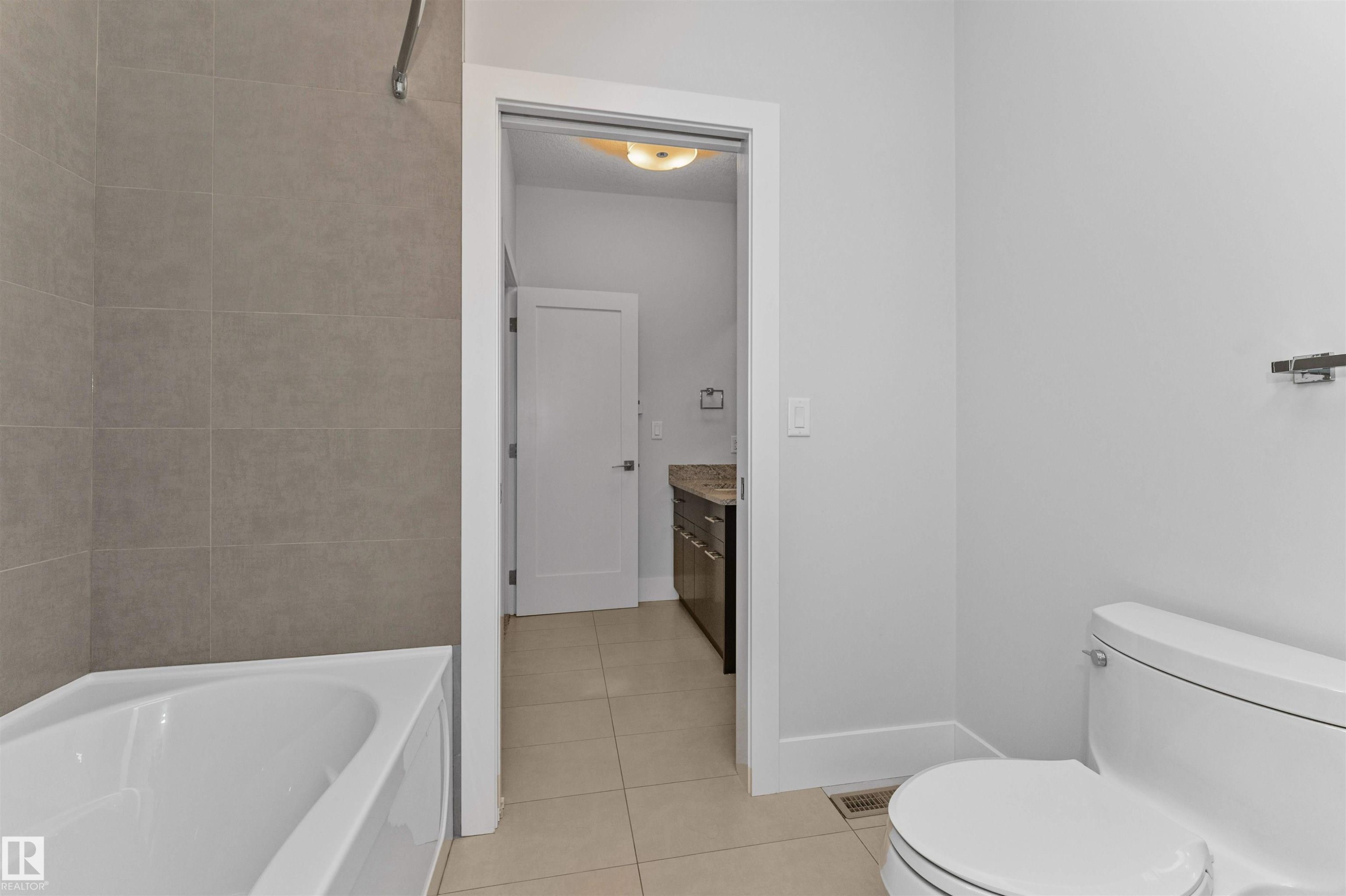 Bathroom featuring a white toilet, light gray wall tile, a white bathtub, and light-colored floor tile - 3310 Watson Bay, Edmonton, AB