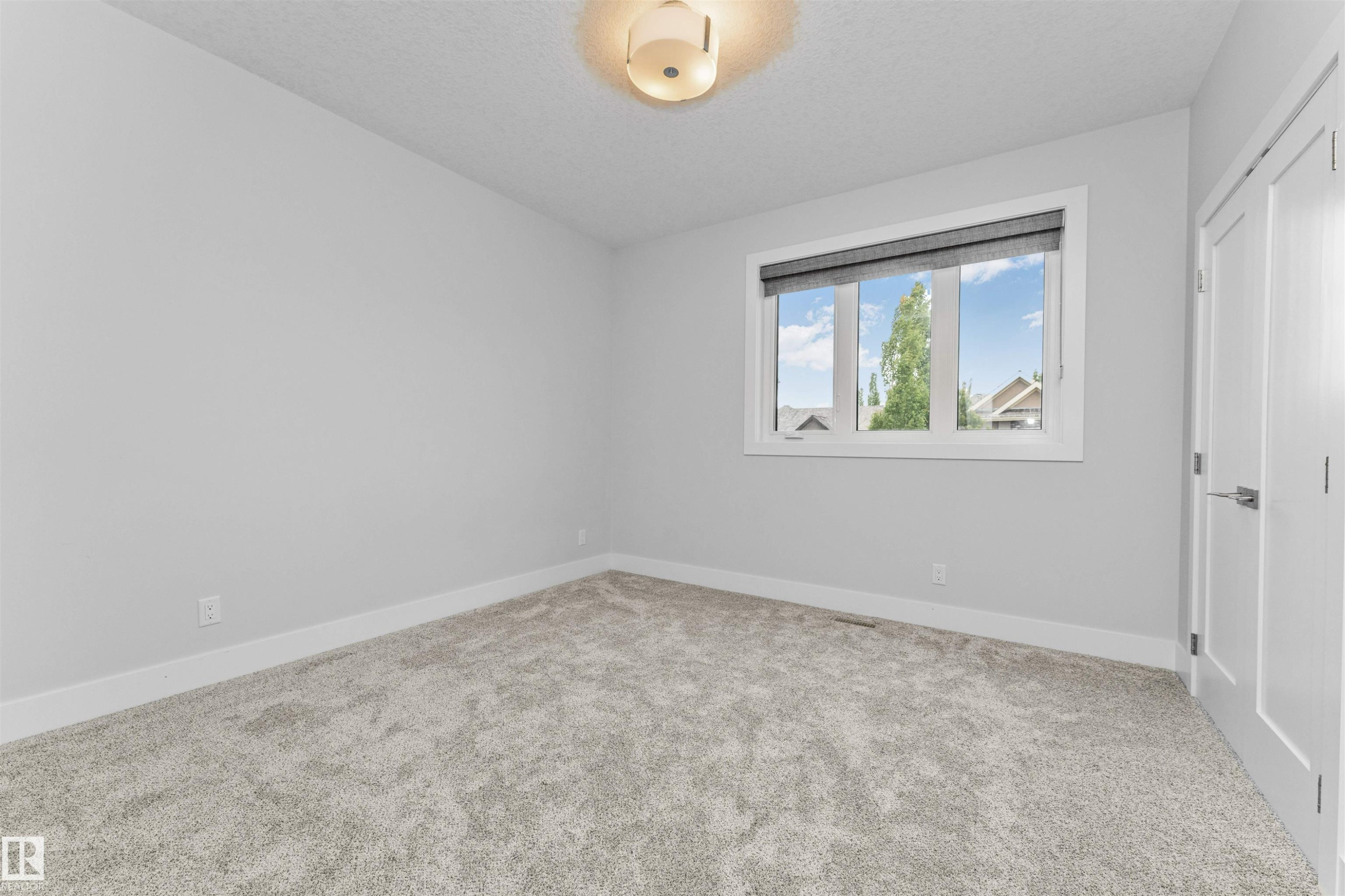Carpeted room featuring a large window with blinds, white trim, a flush mount ceiling light, and a white interior door with a silver handle - 3310 Watson Bay, Edmonton, AB