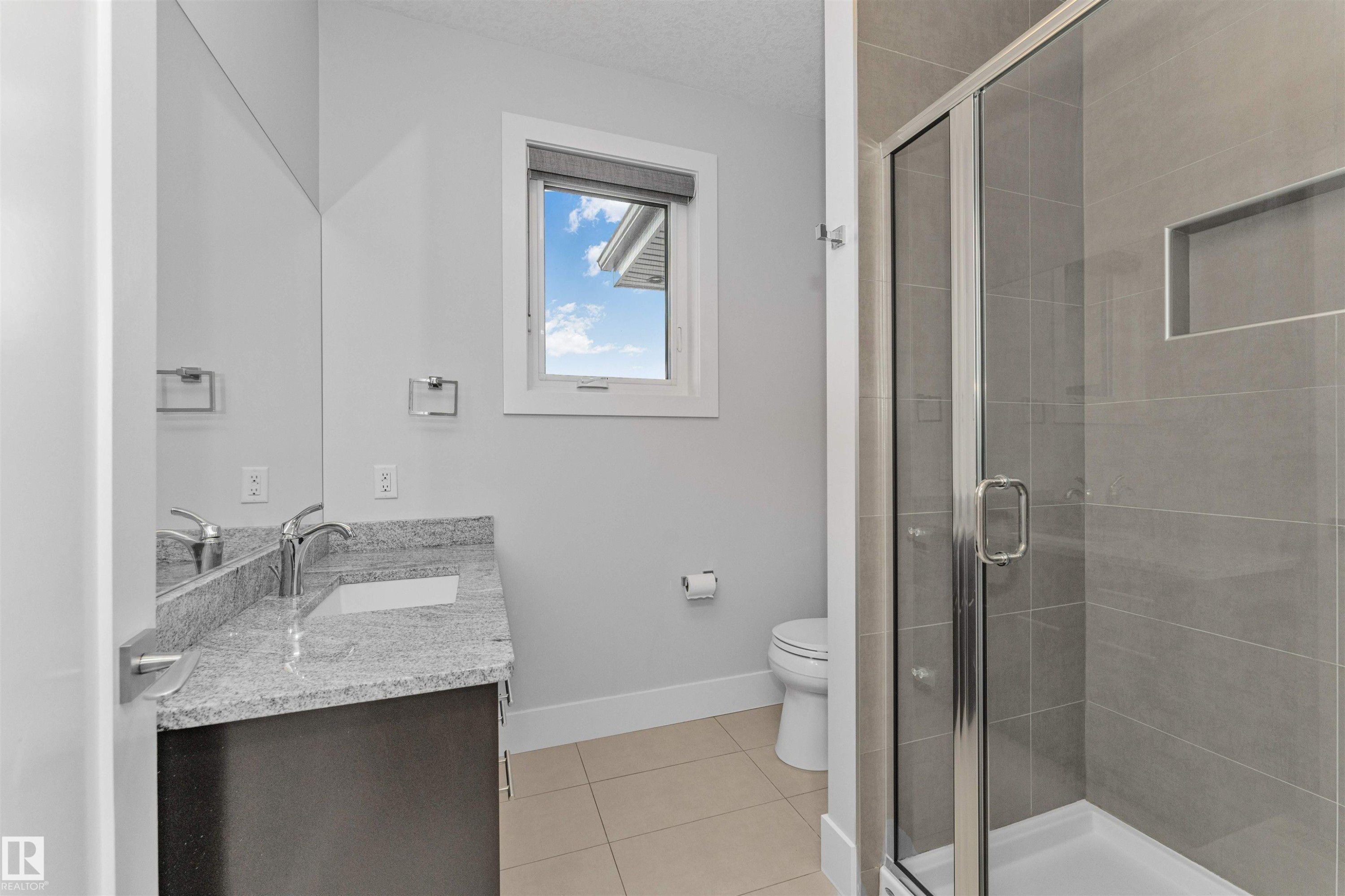 Bathroom featuring a glass-enclosed shower, tiled flooring, vanity with granite countertop and integrated sink, and a framed window - 3310 Watson Bay, Edmonton, AB