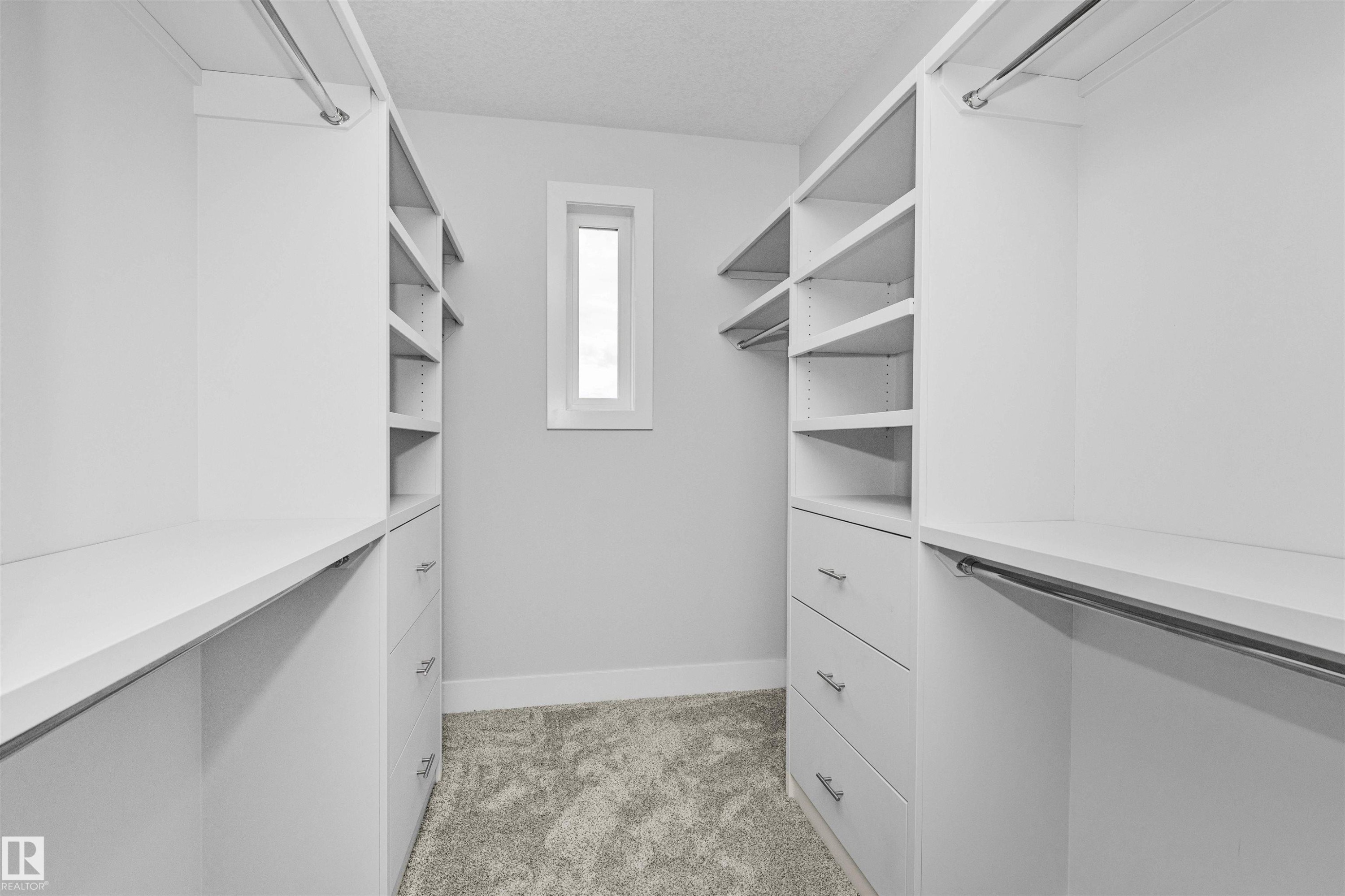 Walk-in closet with custom built-ins featuring white shelving, integrated drawers with brushed nickel hardware, multiple hanging rods, and a window providing natural illumination - 3310 Watson Bay, Edmonton, AB